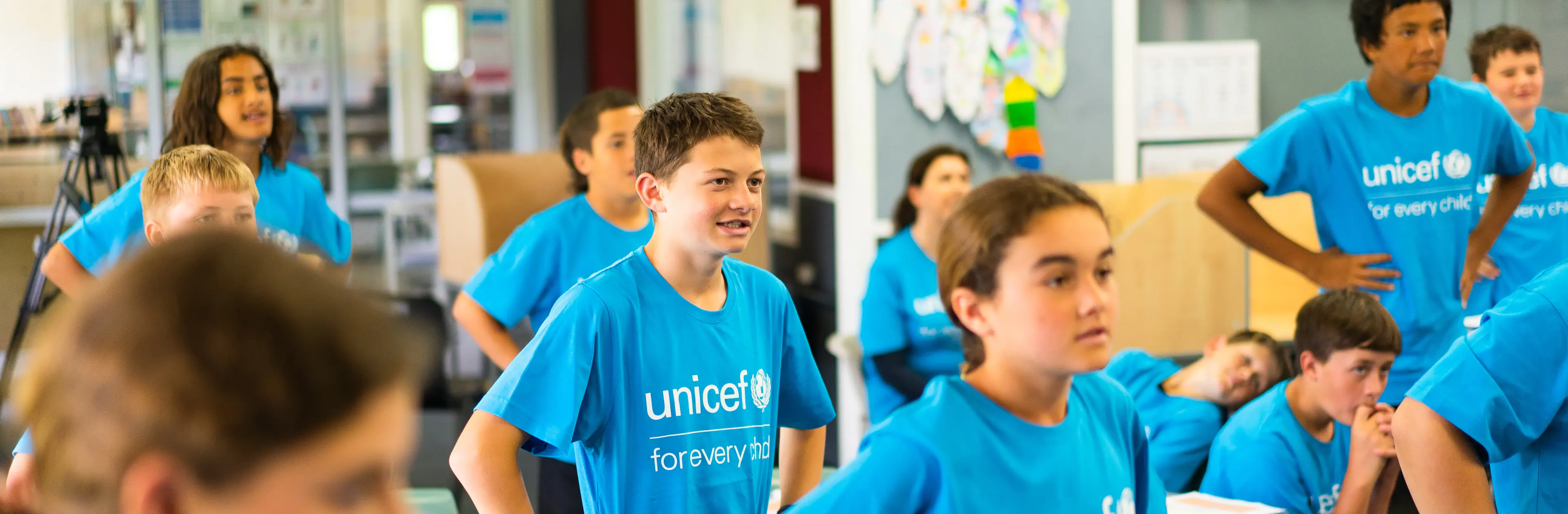 School children at Poipoi School wearing bright blue UNICEF "for every child" t-shirts while standing in a classroom during a 2022 visit.