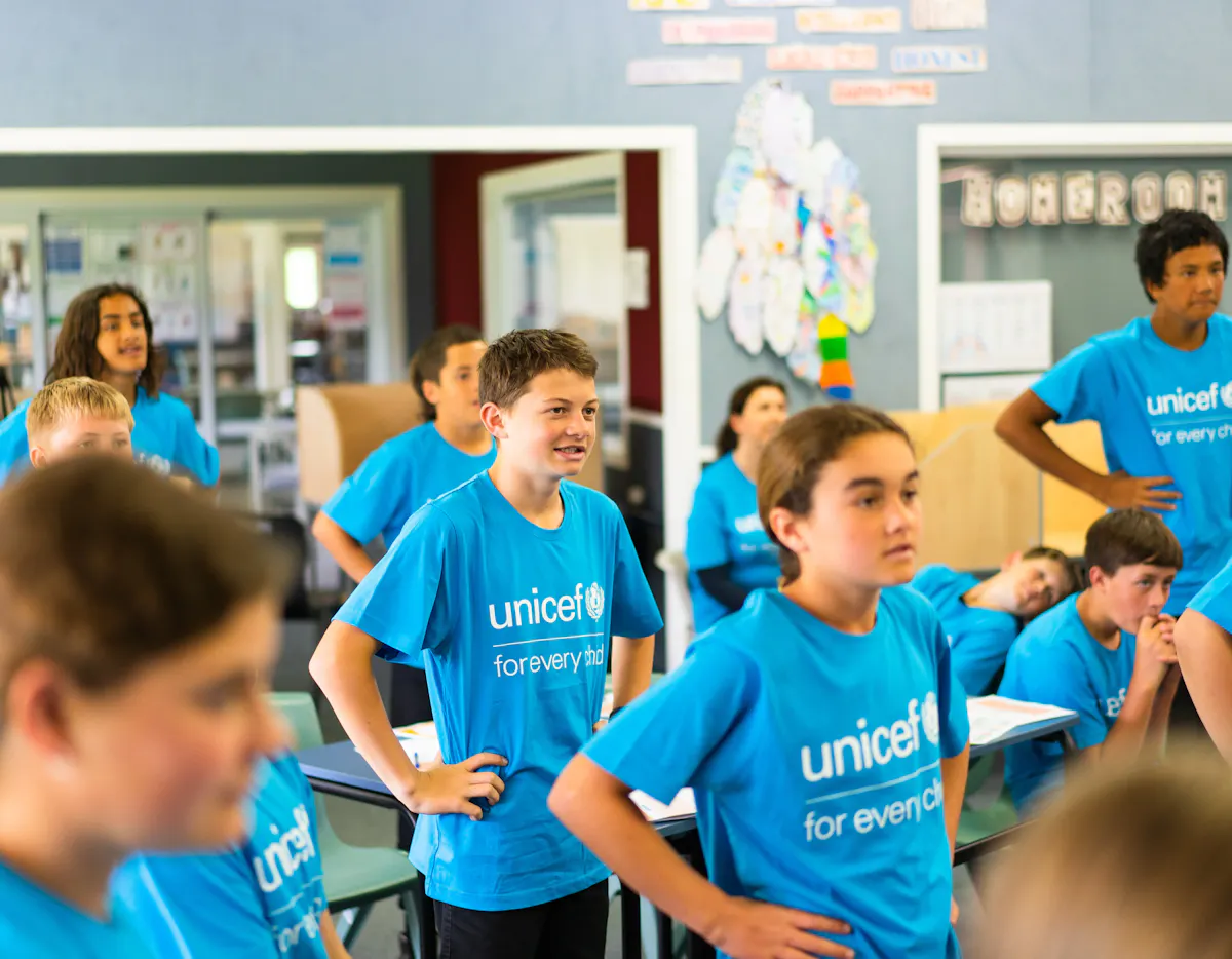 School children at Poipoi School wearing bright blue UNICEF "for every child" t-shirts while standing in a classroom during a 2022 visit.