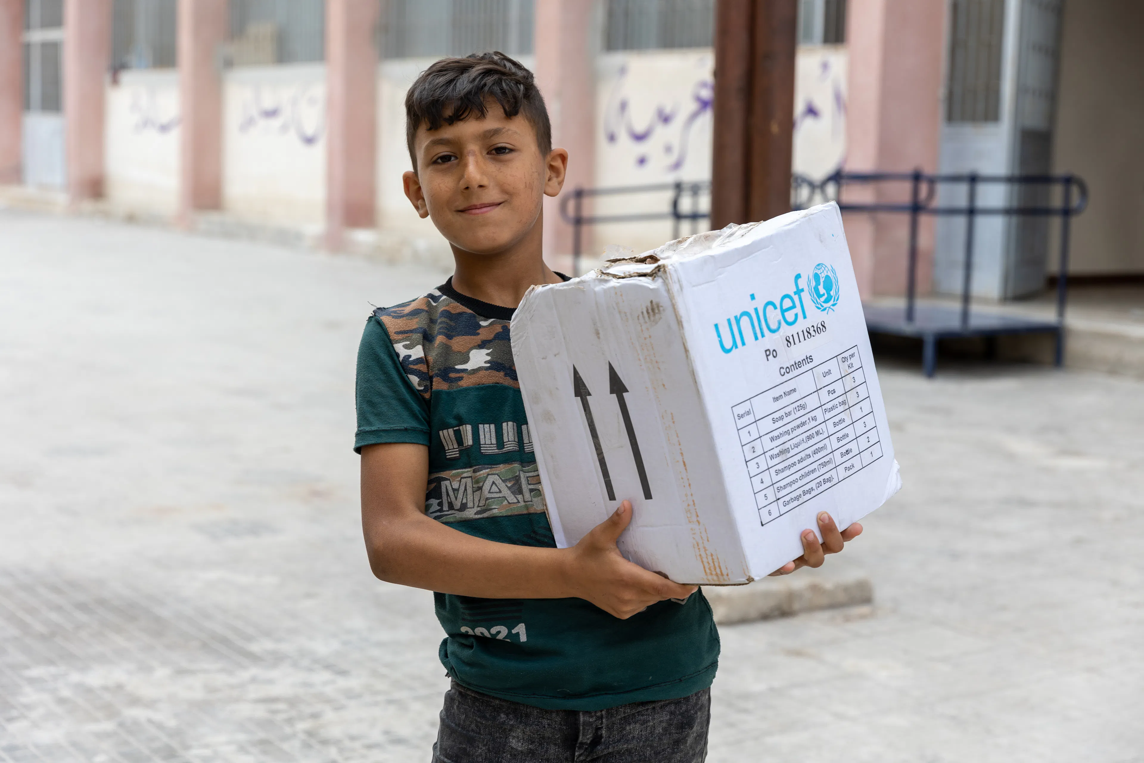 Abed, 10, carries his family hygiene box, distributed by UNICEF, at Bader Shaker Al Sayeb school-turned shelter in Aleppo city, Syria, on 14 June 2023.