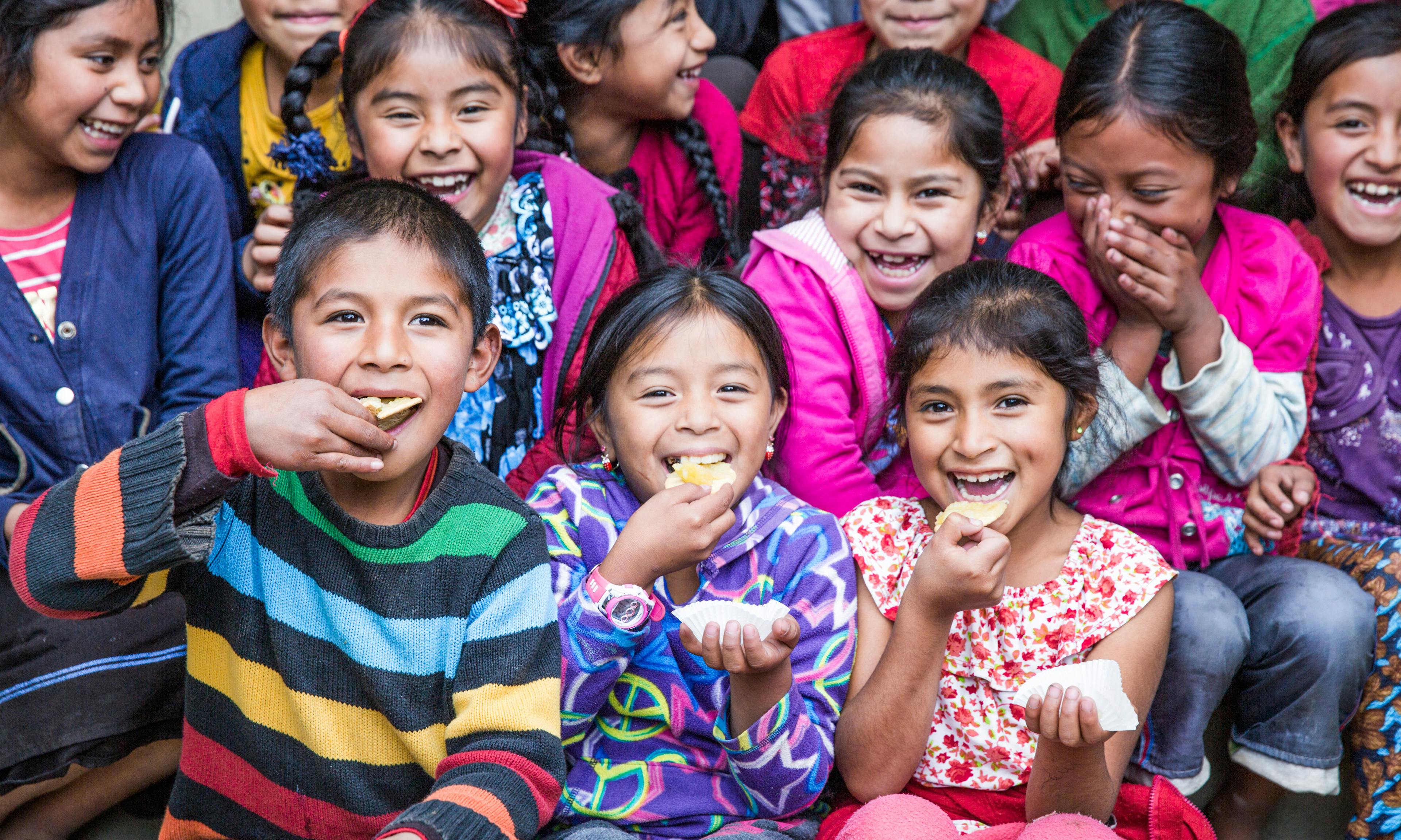 A group of children laughing and smiling while they eat muffins