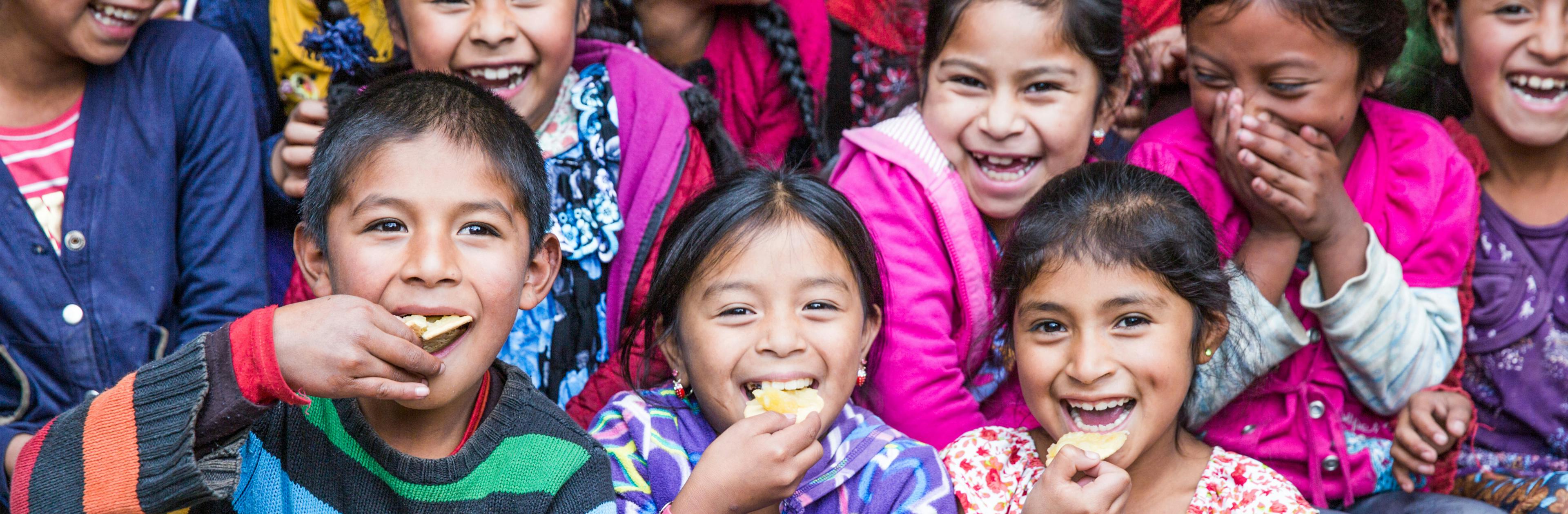 A group of children laughing and smiling while they eat muffins