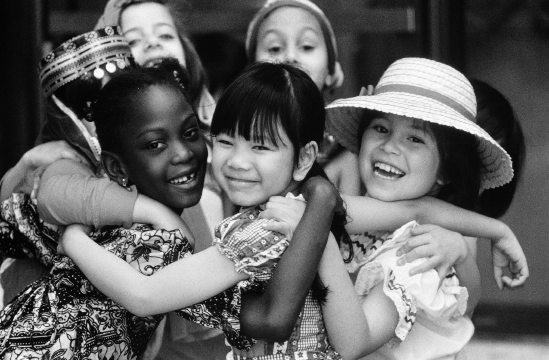 In 1979 in the United States of America, a group of smiling girls embrace.  The girls, dressed in traditional costumes of their homelands, are standing outside the United Nations International School in New York City. 