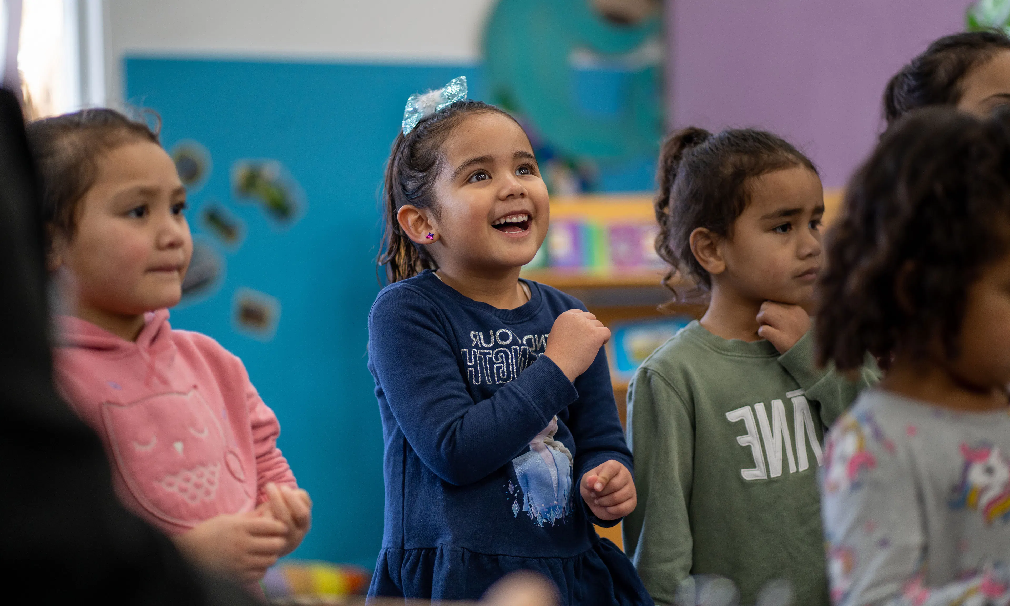young children in sit together, smiling and laughing. They are dressed in warm hoodies and jackets, capturing a joyful moment of friendship and wellbeing