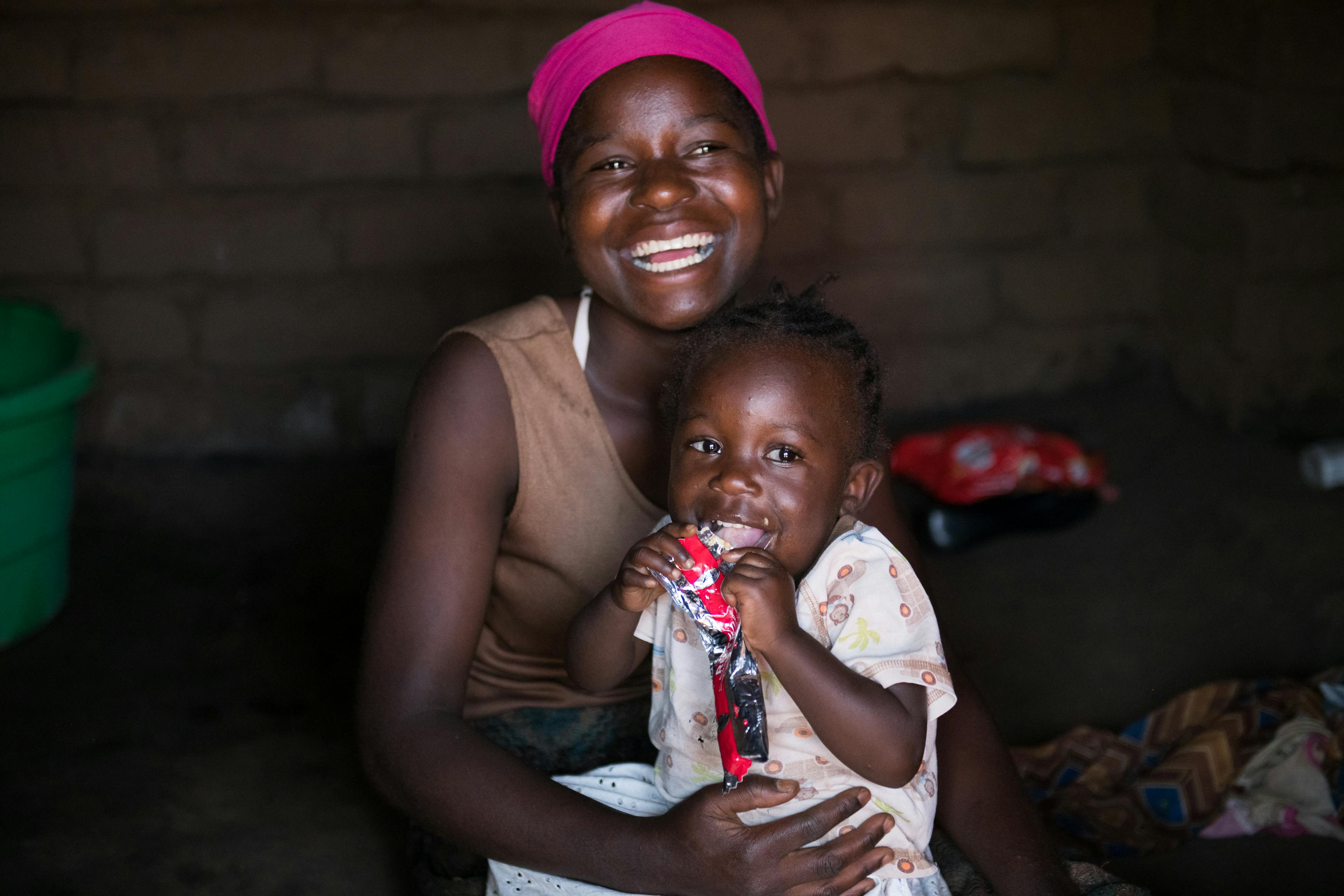 20-year-old Edna Maunde smiles as her daughter, 2 year 4 months old Christina Cosmas eats RUTF at their home in Mavila Village, Zomba, southern Malawi on Thursday, 8 June 2023.