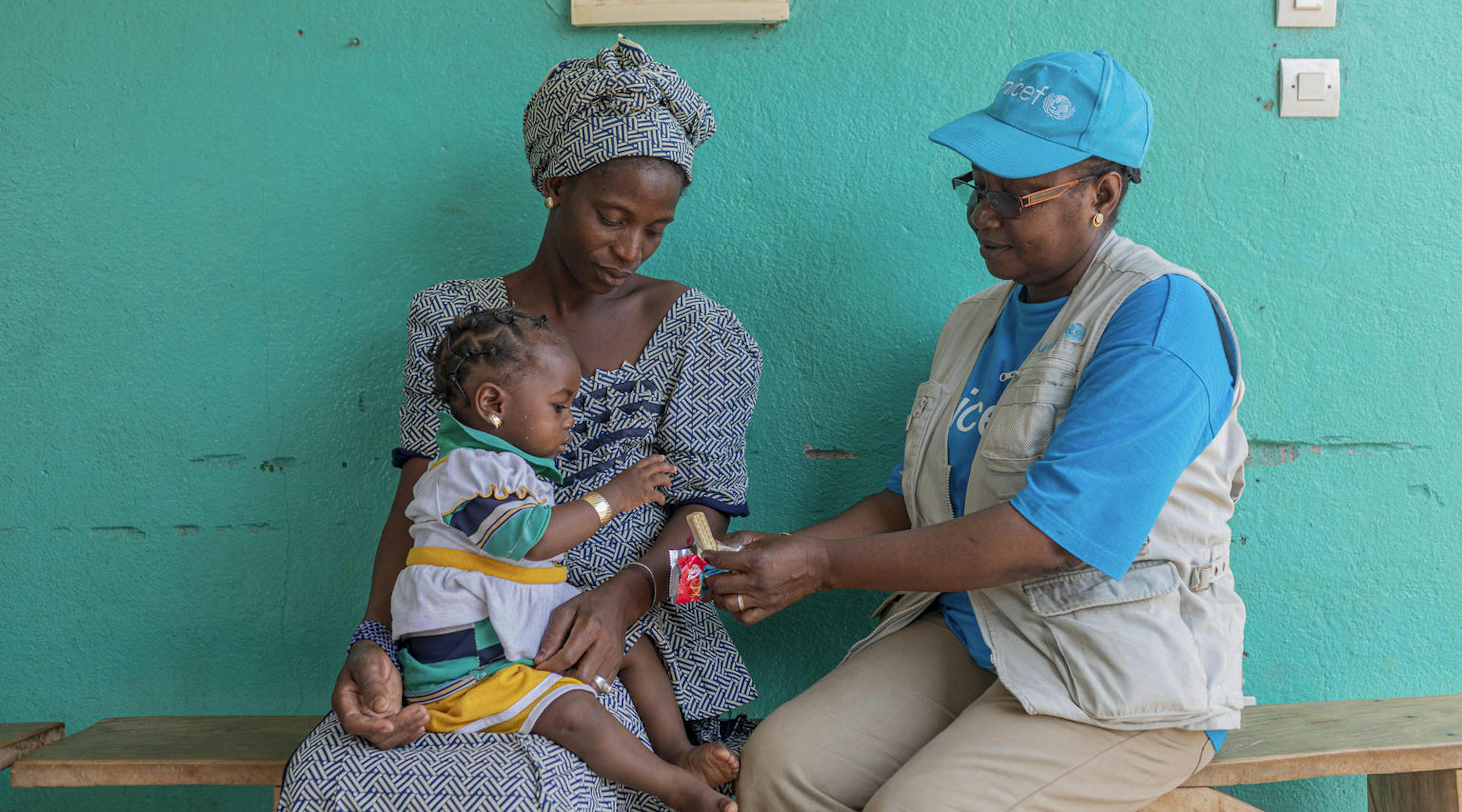 UNICEF representative Mariam Sissoko gives high-energy biscuits to Malado Diarra (1) as she sits on her mother's lap at a UNICEF supported Community Health Centre in Mali.