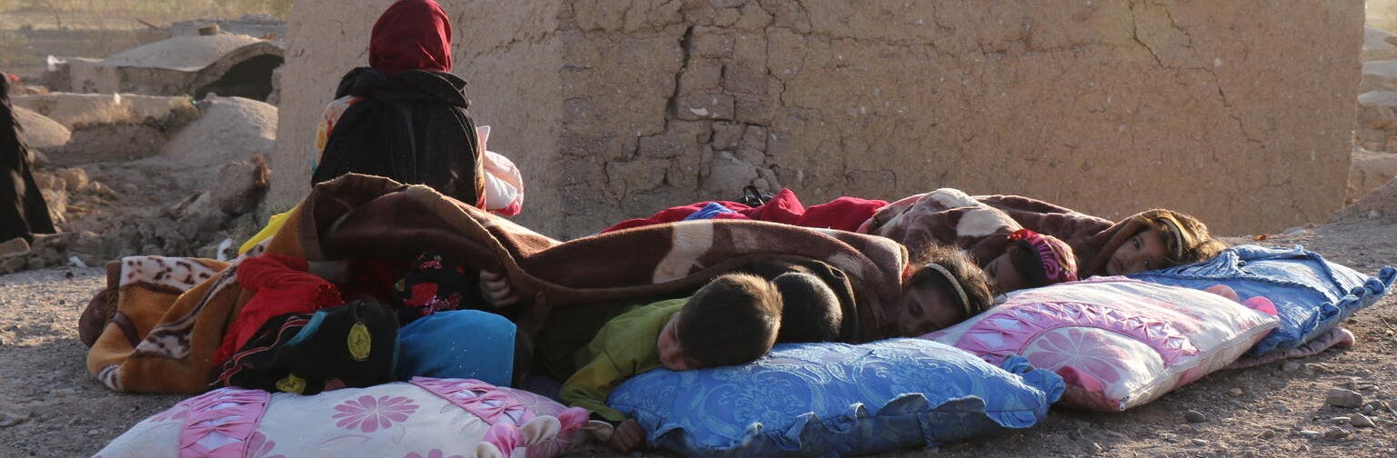 Afghan children rest under a blanket beside damaged houses after the earthquake shook their village in Herat province