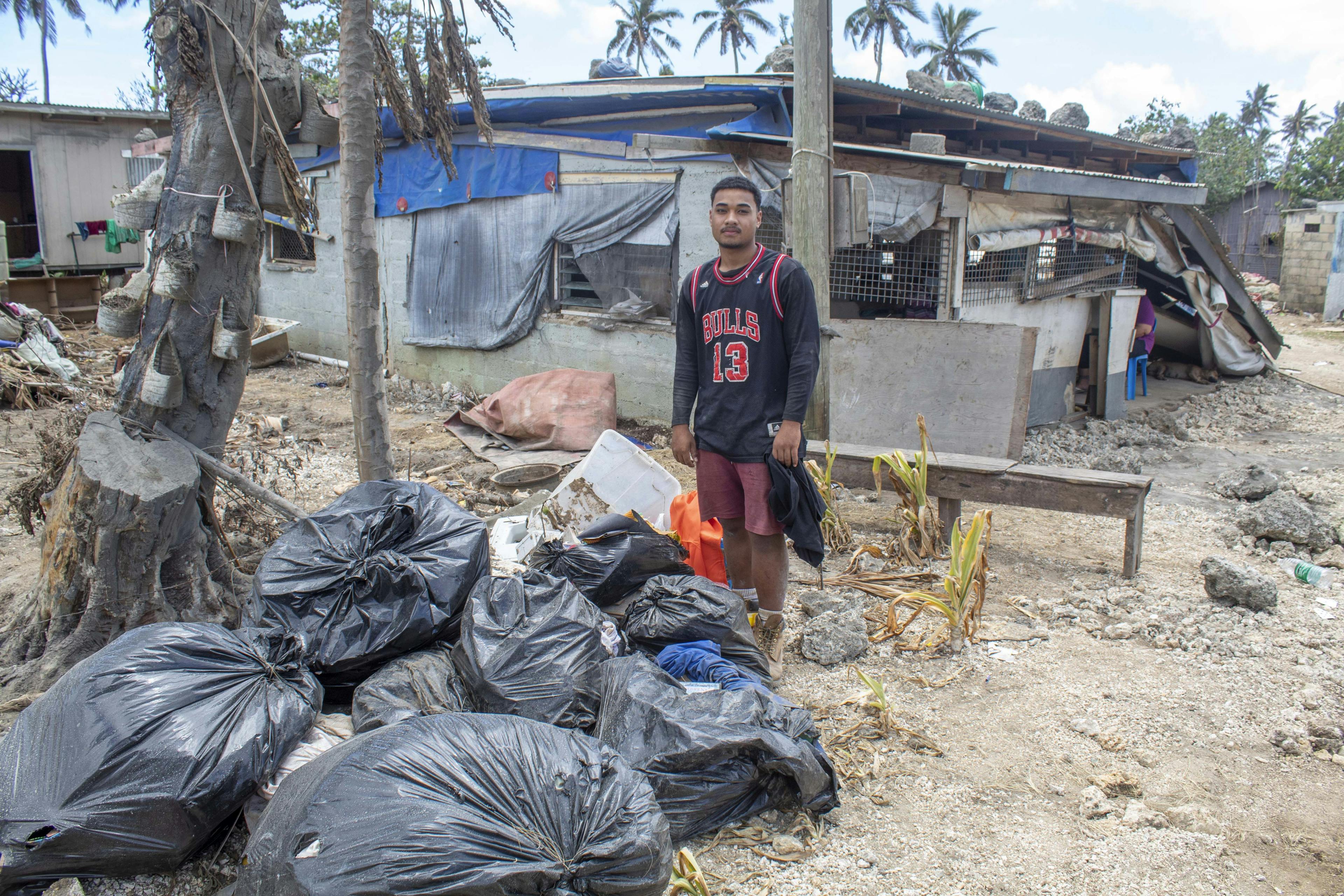 On 22 January 2022, (left) Sione Falani Kuli Ha'apai, 18, stands in front of his home in Sopu on Tongatapu, Tonga’s main island, showing the damage caused by the Hunga Tonga-Hunga Ha’apai underwater volcano eruption and tsunami. Esther Kuli Ha'apai, 52, is seen in the background on the right.