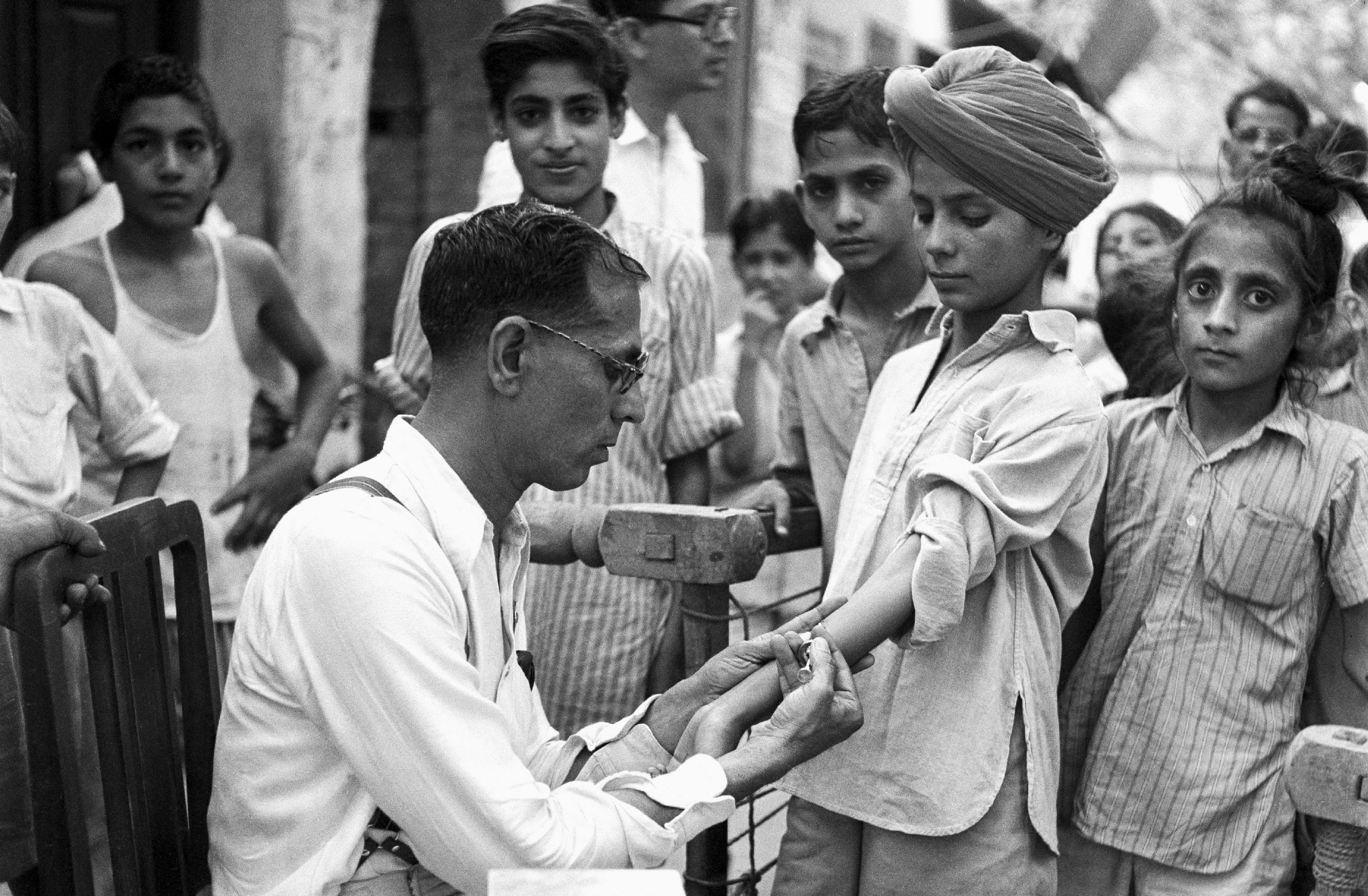 Circa 1956 in India, a Norwegian doctor from the World Health Organization (WHO) tests a boy for tuberculosis at an outdoor street site in New Delhi, the capital. If the test is negative, the boy will be vaccinated to ensure that he does not contract the disease. 