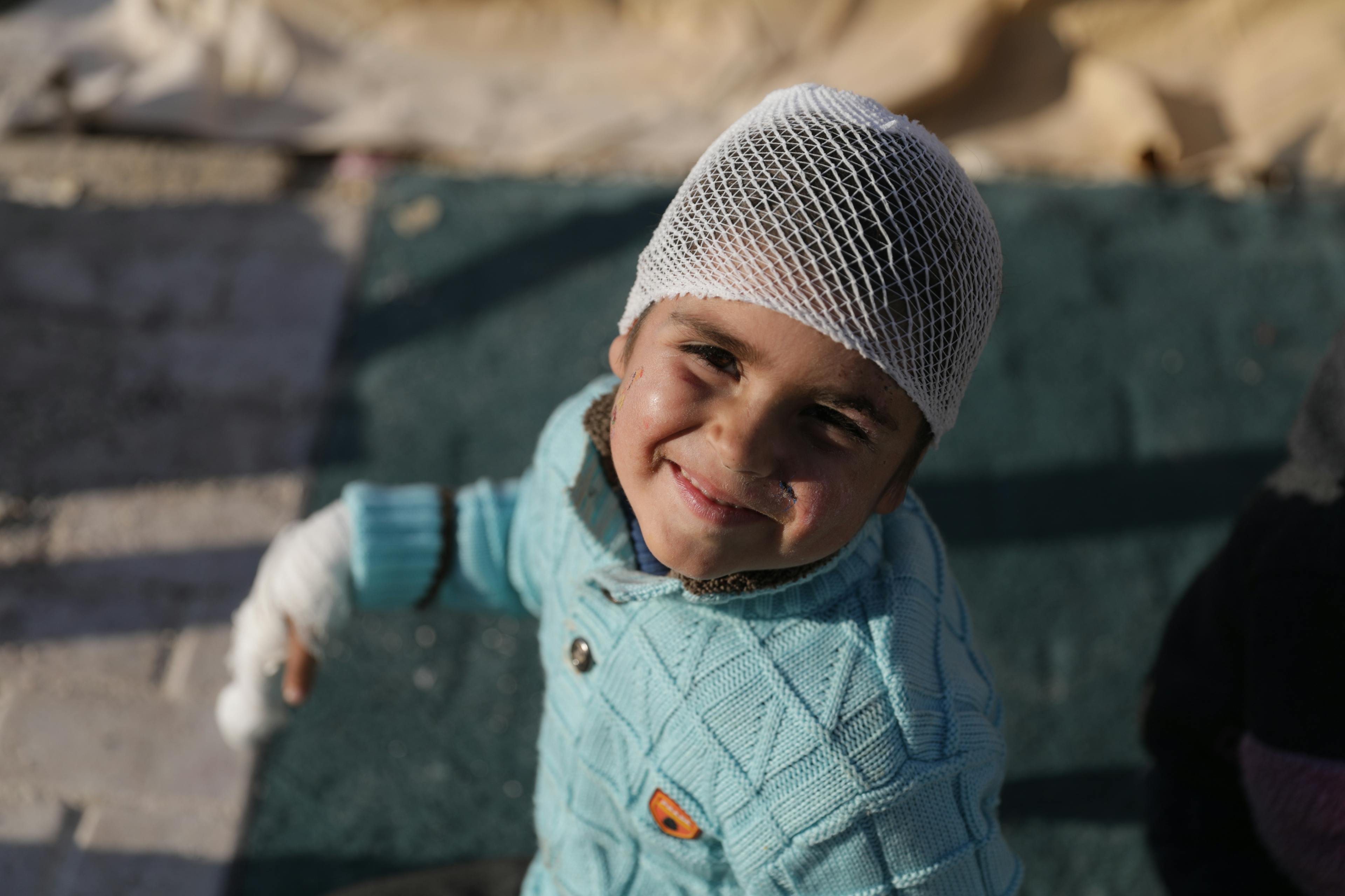 A young girl with a bandage on her head smiles at the camera