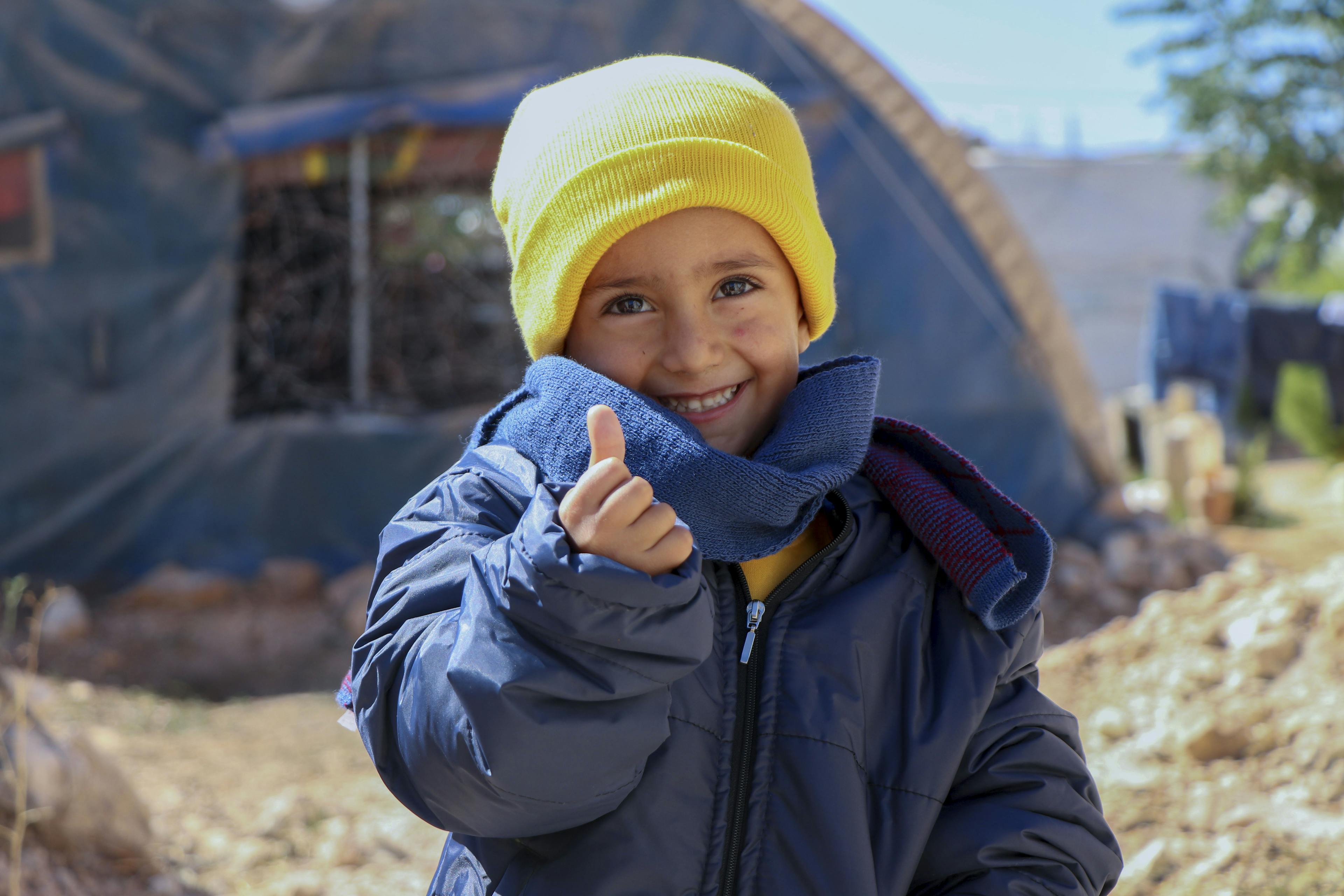 Contact Us- 4-year-old Rashid smiles broadly while enjoying his new winter clothes distributed by UNICEF in Fafin camp, north rural Aleppo