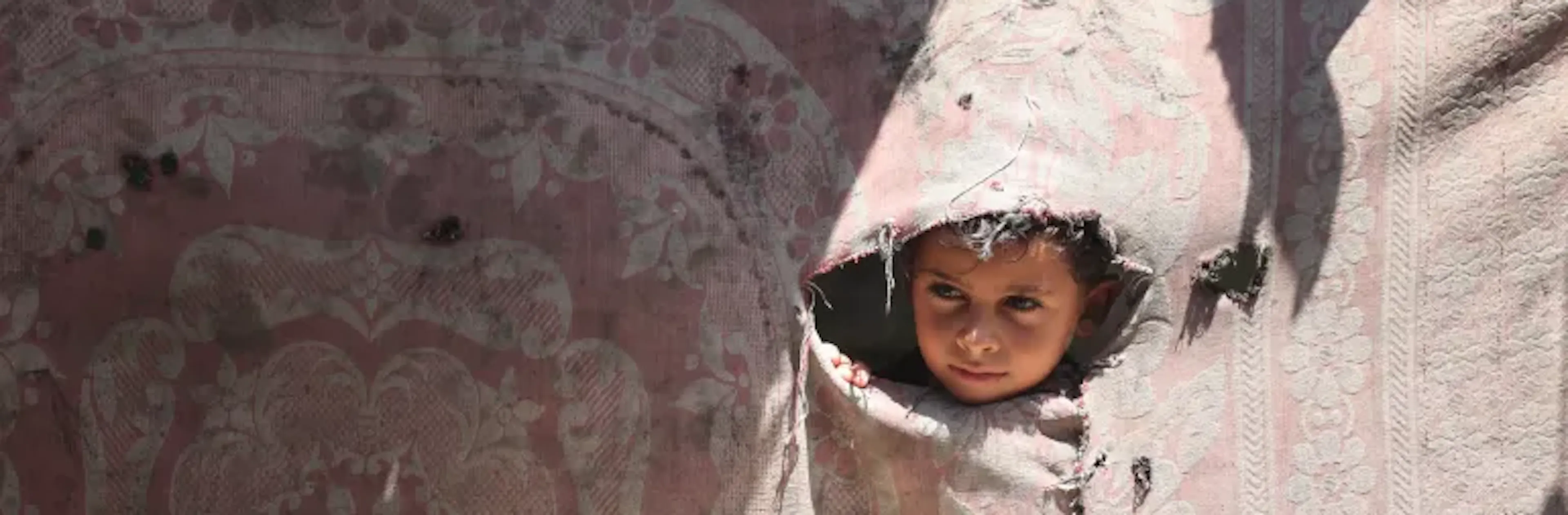 Jasser, a 7-year-old child from Gaza, looks out of one of the broken walls of a tent.