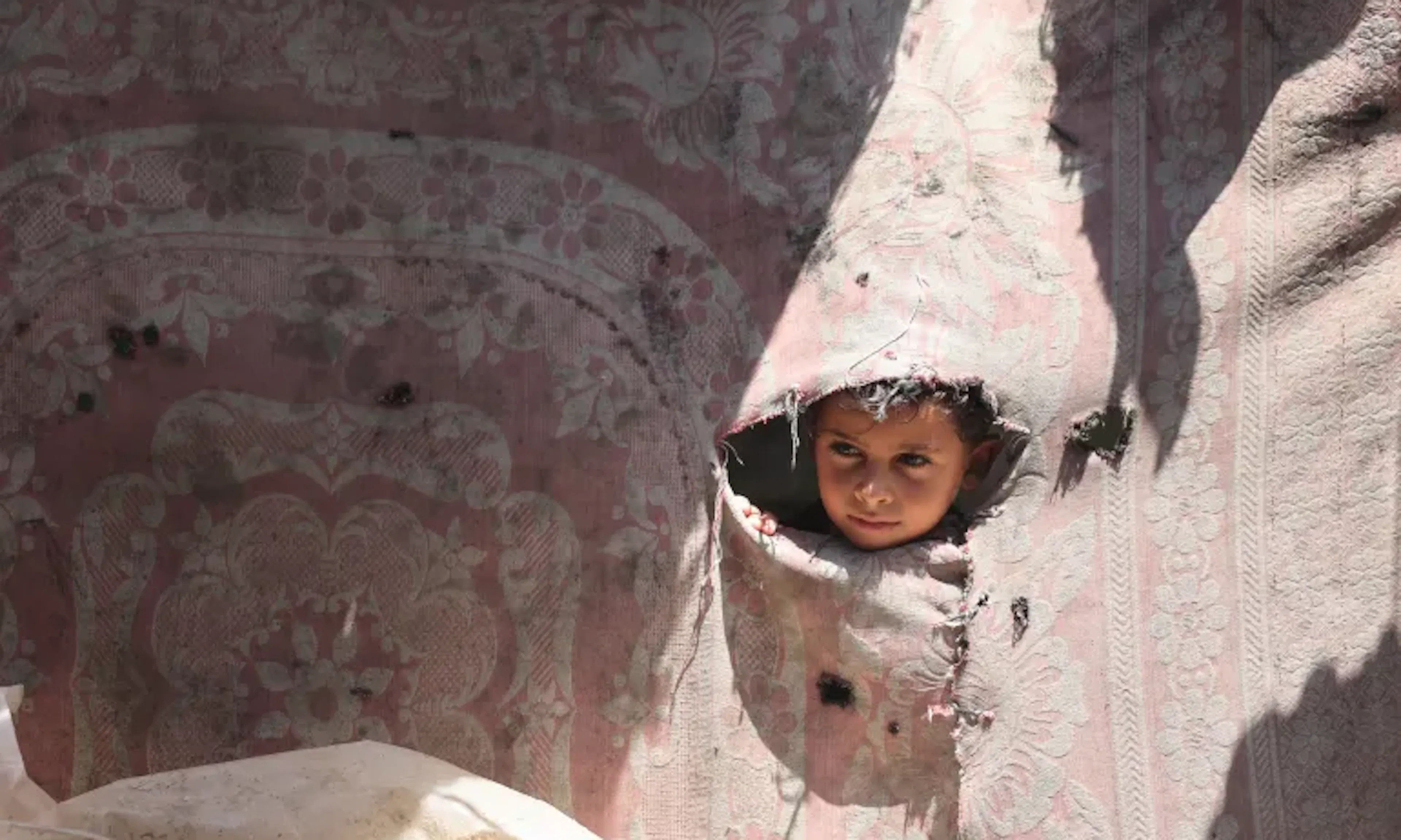 Jasser, a 7-year-old child from Gaza, looks out of one of the broken walls of a tent.