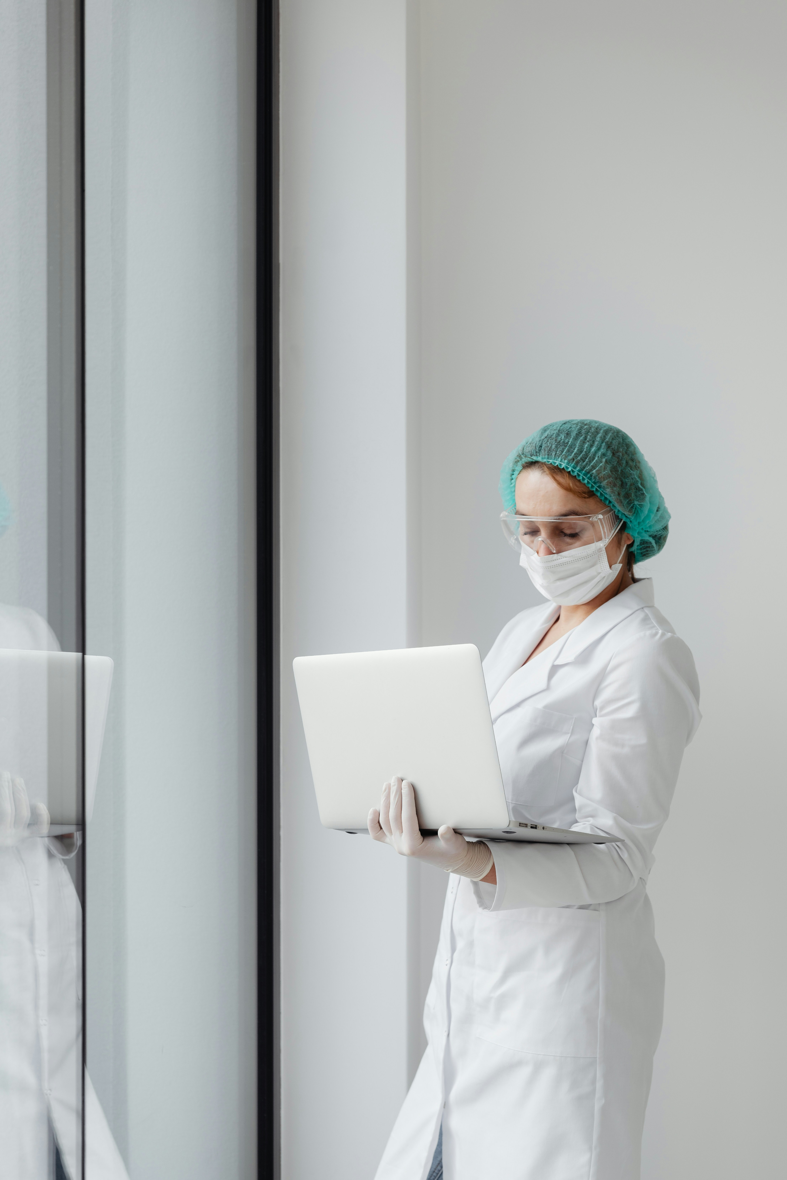 A scientist dressed in a white lab coat examines data on a laptop screen that she is carrying