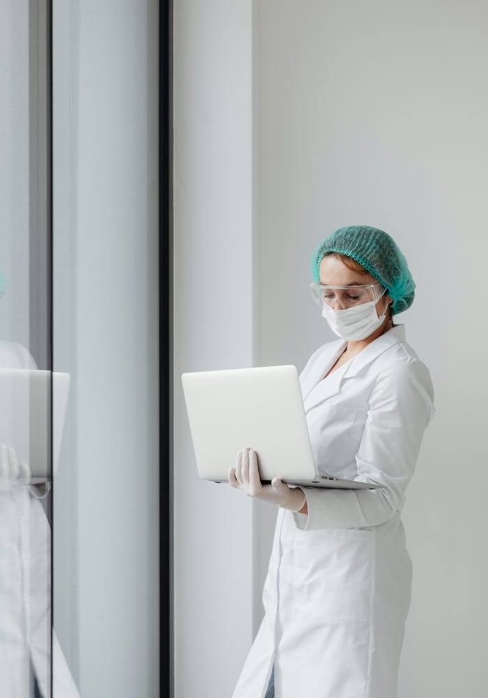 A scientist dressed in a white lab coat examines data on a laptop screen that she is carrying