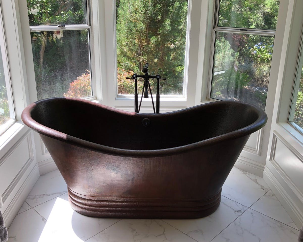 A custom freestanding copper bathtub inside of a bathroom surrounded by outdoor windows