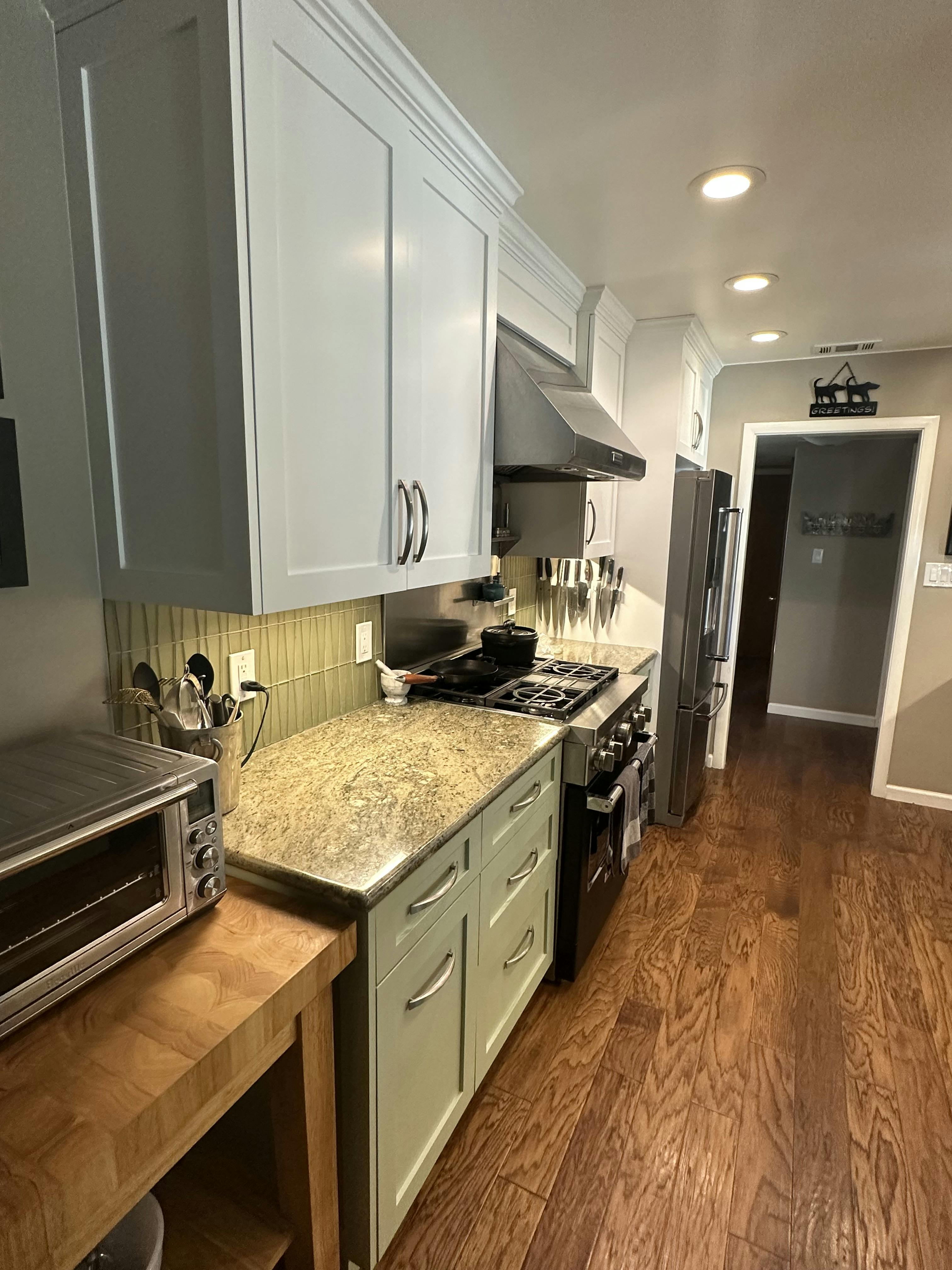 Kitchen corner showcasing gray cabinets and a gas stove, with under-cabinet lighting casting a warm glow over the beige tiled backsplash and wooden countertops.