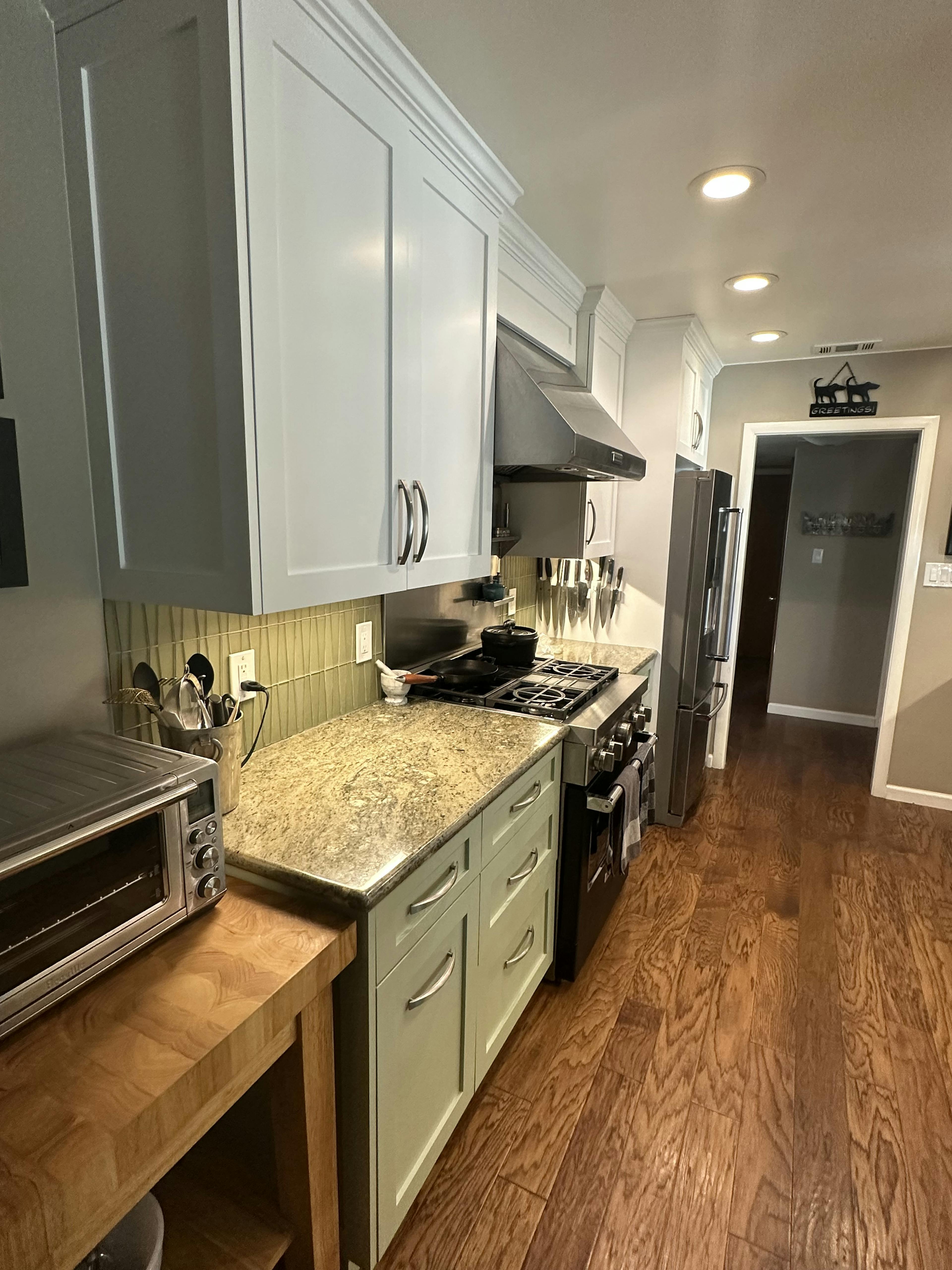 Kitchen corner showcasing gray cabinets and a gas stove, with under-cabinet lighting casting a warm glow over the beige tiled backsplash and wooden countertops.