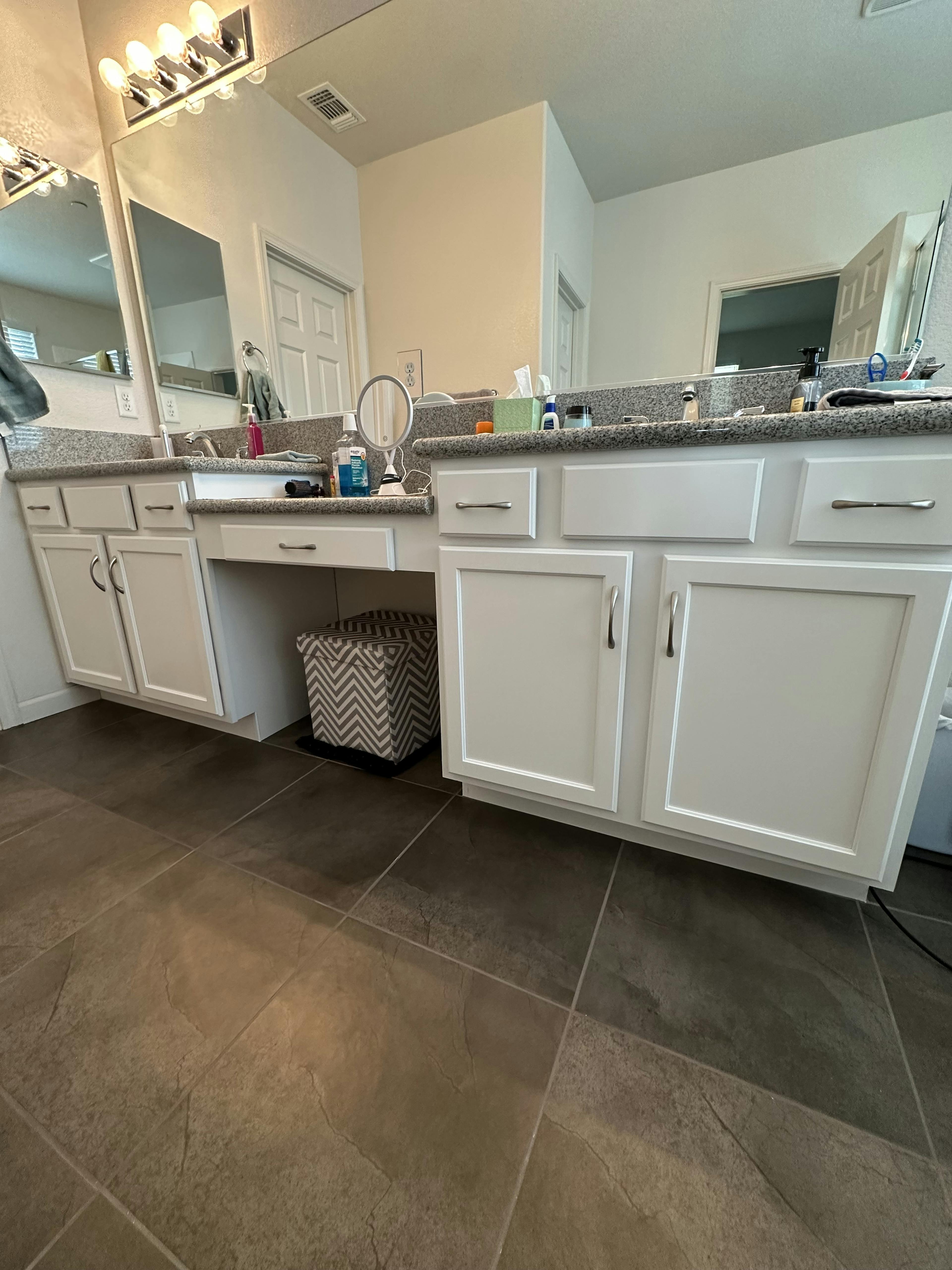 A well-lit bathroom vanity with dual sinks, large mirrors, and a granite countertop.