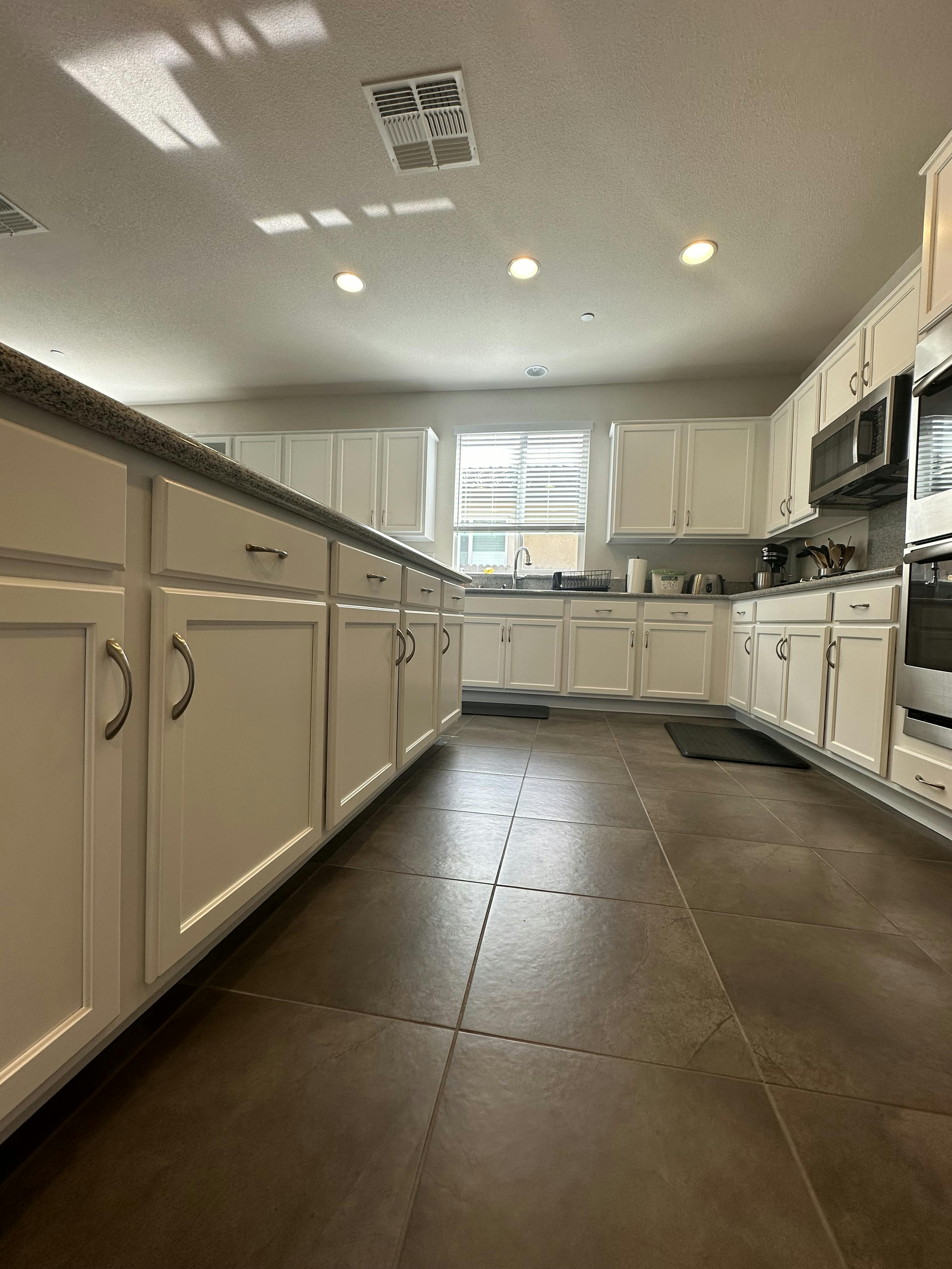 A spacious kitchen with white cabinetry, a marbled counter, and a dark gray island.