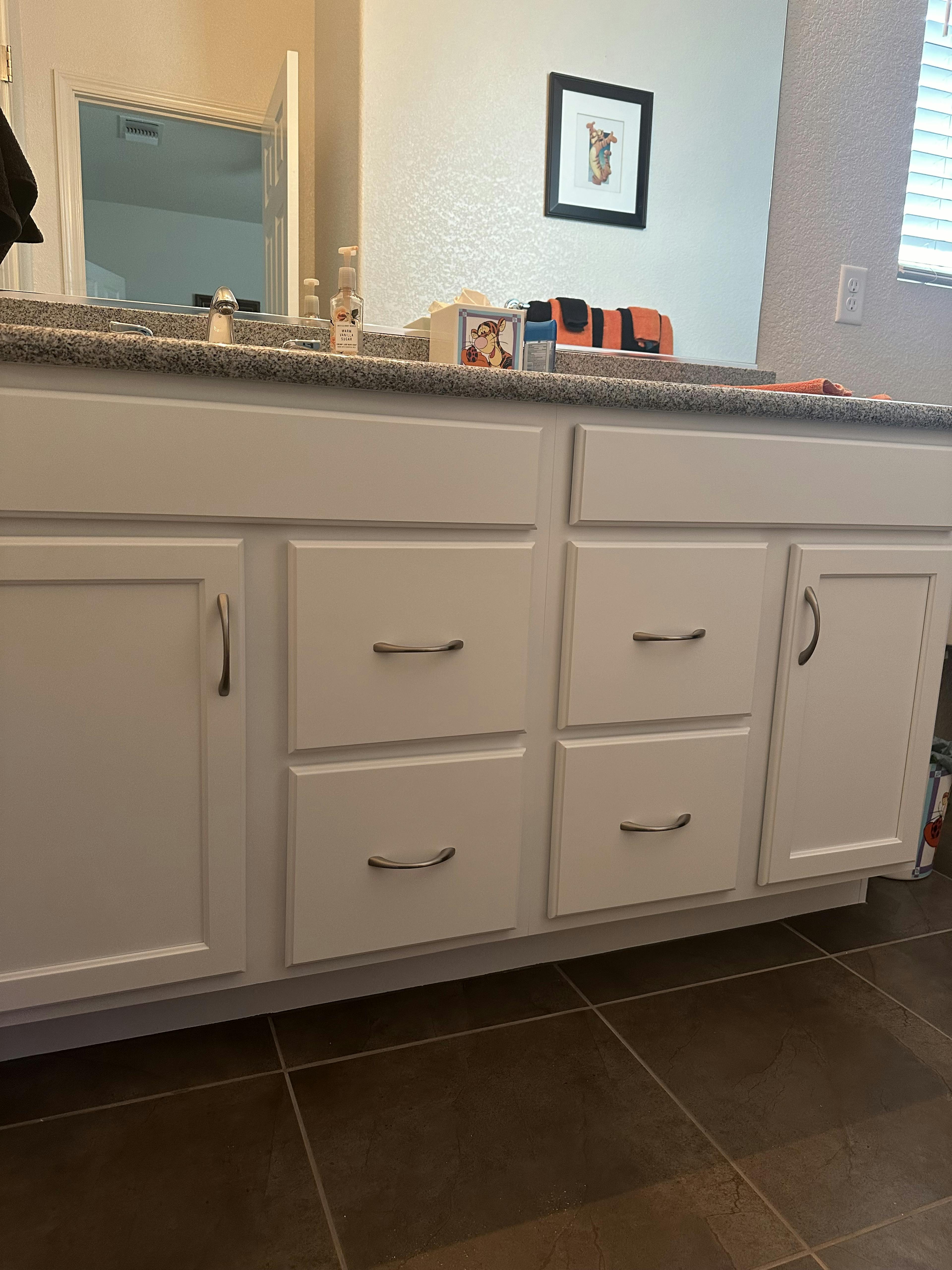 The lower half of the bathroom vanity showing cabinets and drawers on a tiled floor.