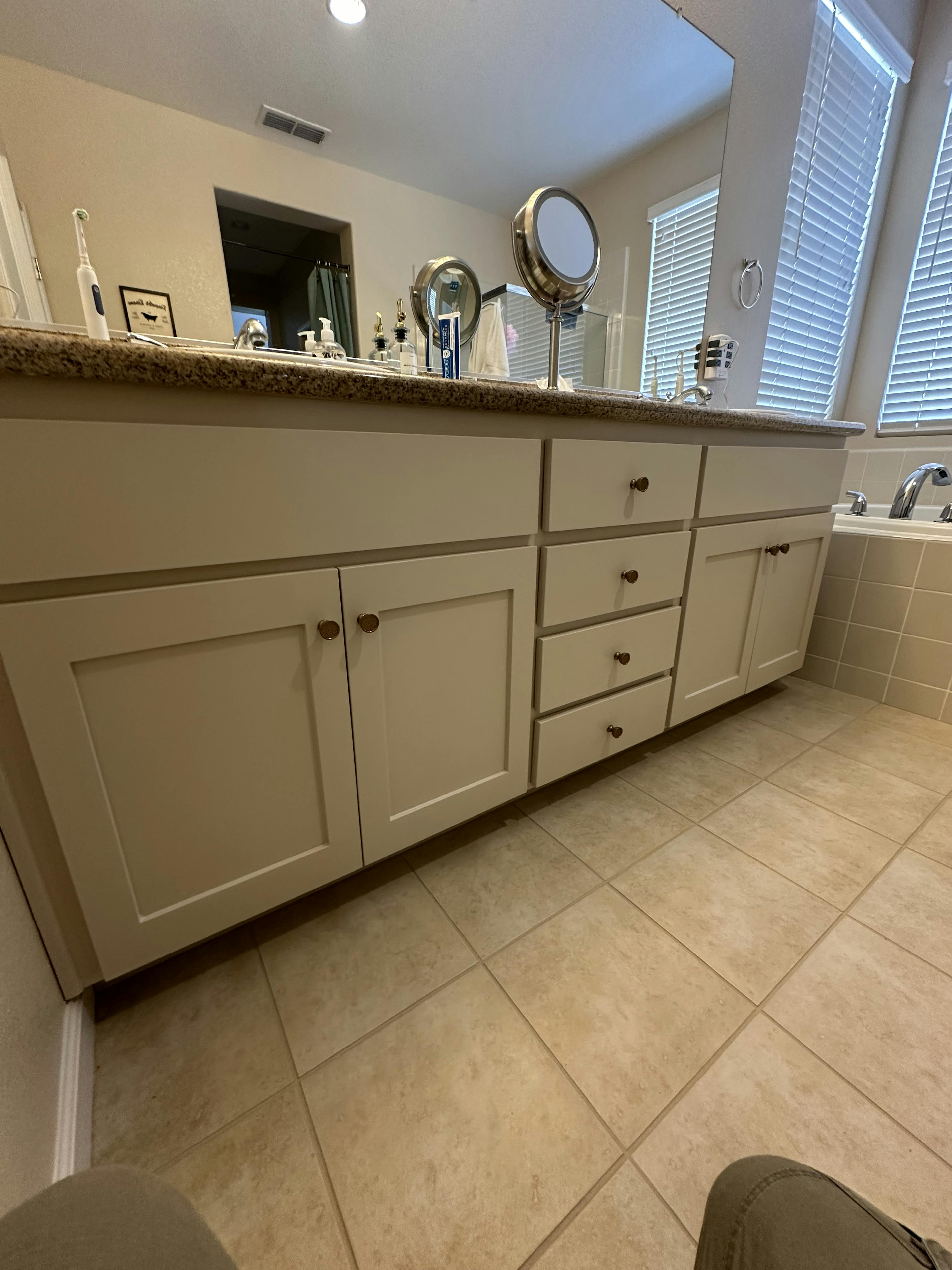 A spacious bathroom vanity featuring a full mirror, granite countertop, and white cabinetry filled with personal care items and colorful hand towels.