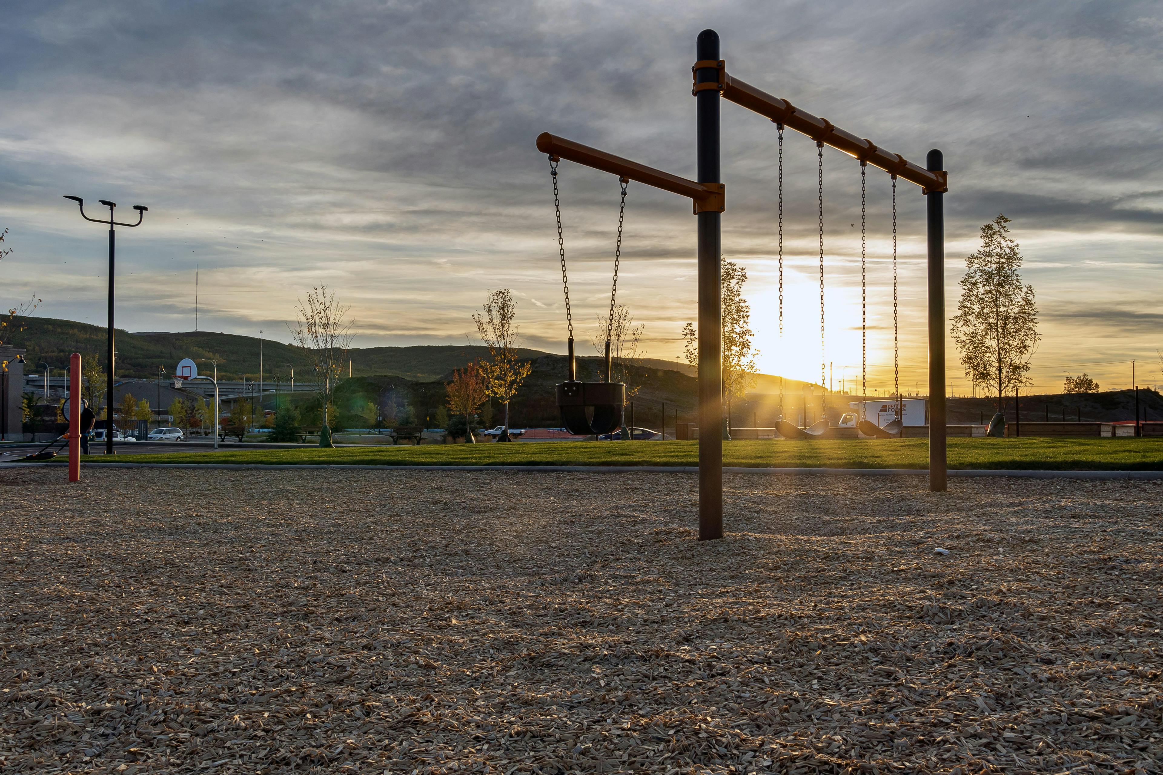 A swing set at a playground, photographed at sunset.