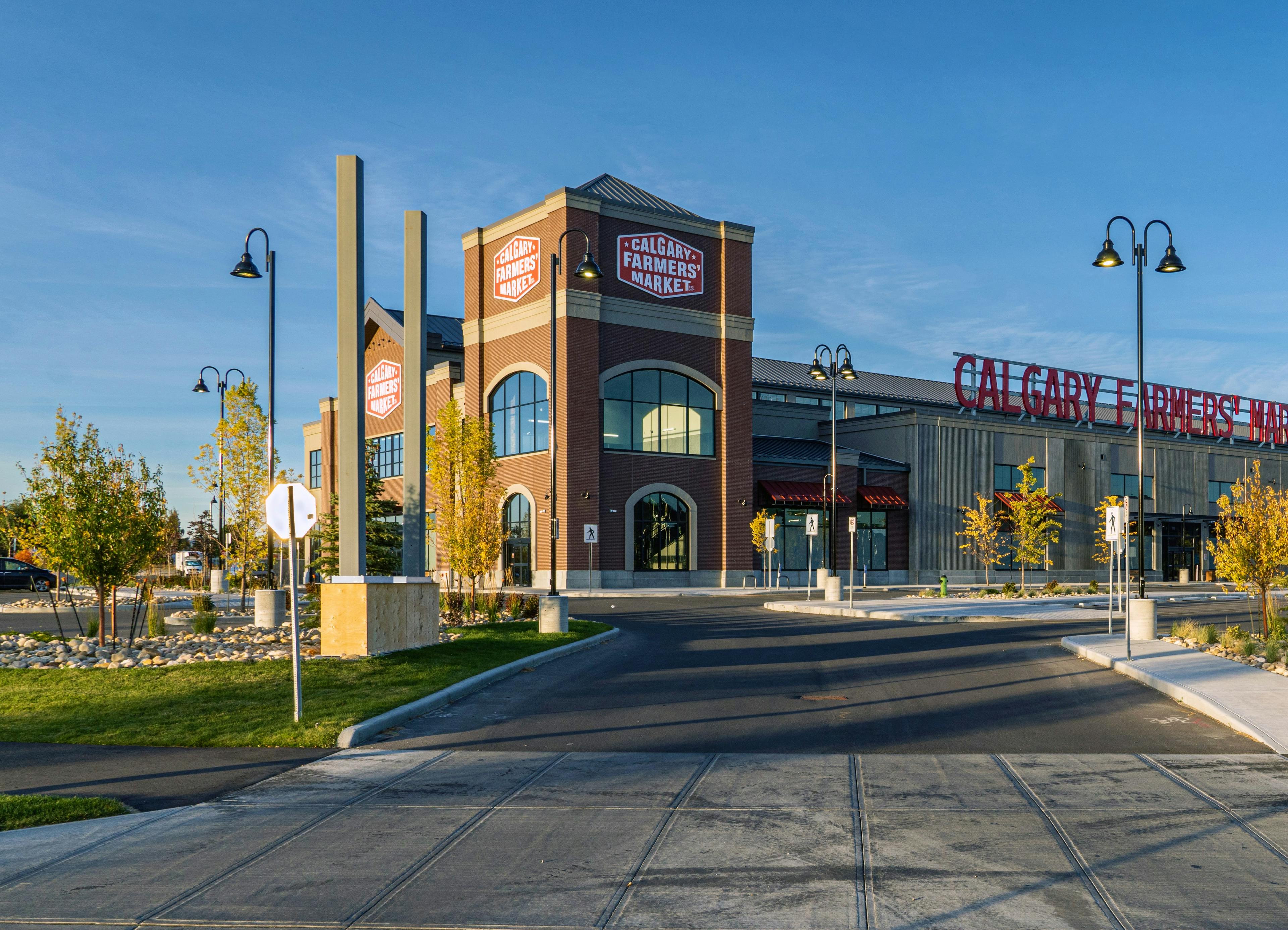 A large building with a brick facade, with large signs reading Calgary Farmers' Market, as viewed in evening light.