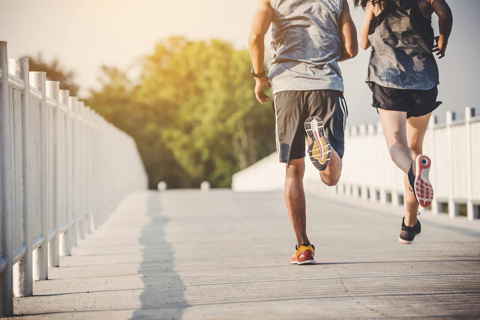 Two people jog along a bridge, toward green trees