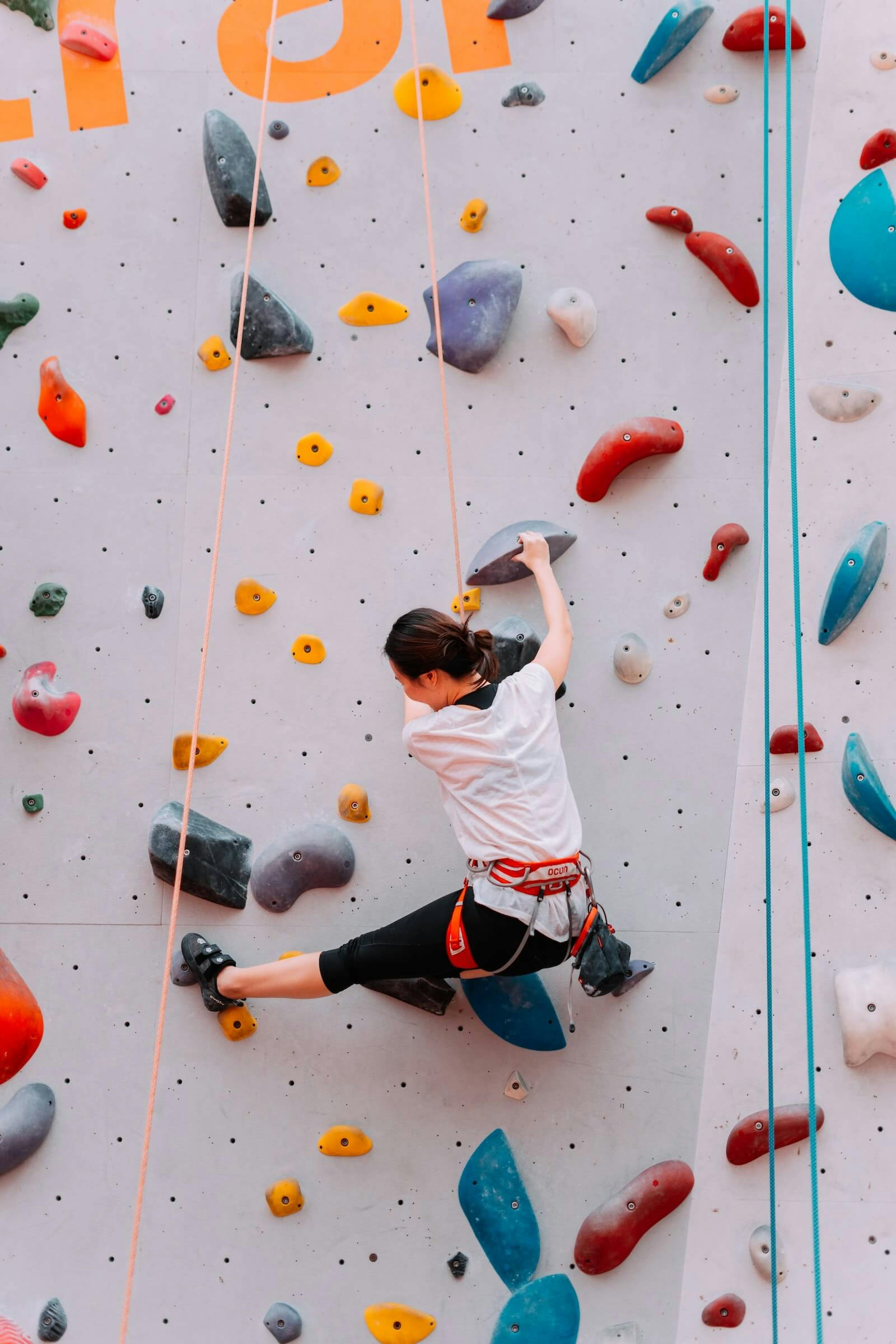 A woman in a harness scales a tall climbing wall