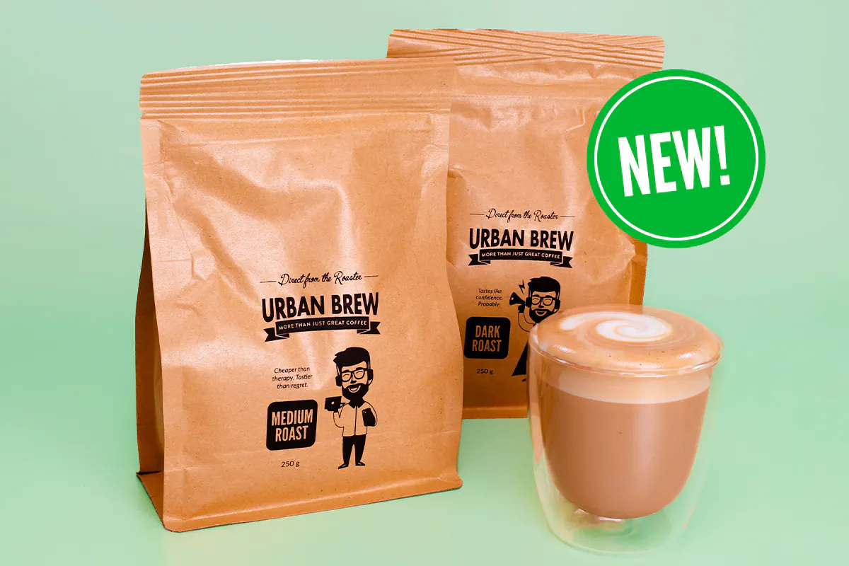 New Urban Brew 250g Medium and Dark Roast bags beside a glass of cafe latte