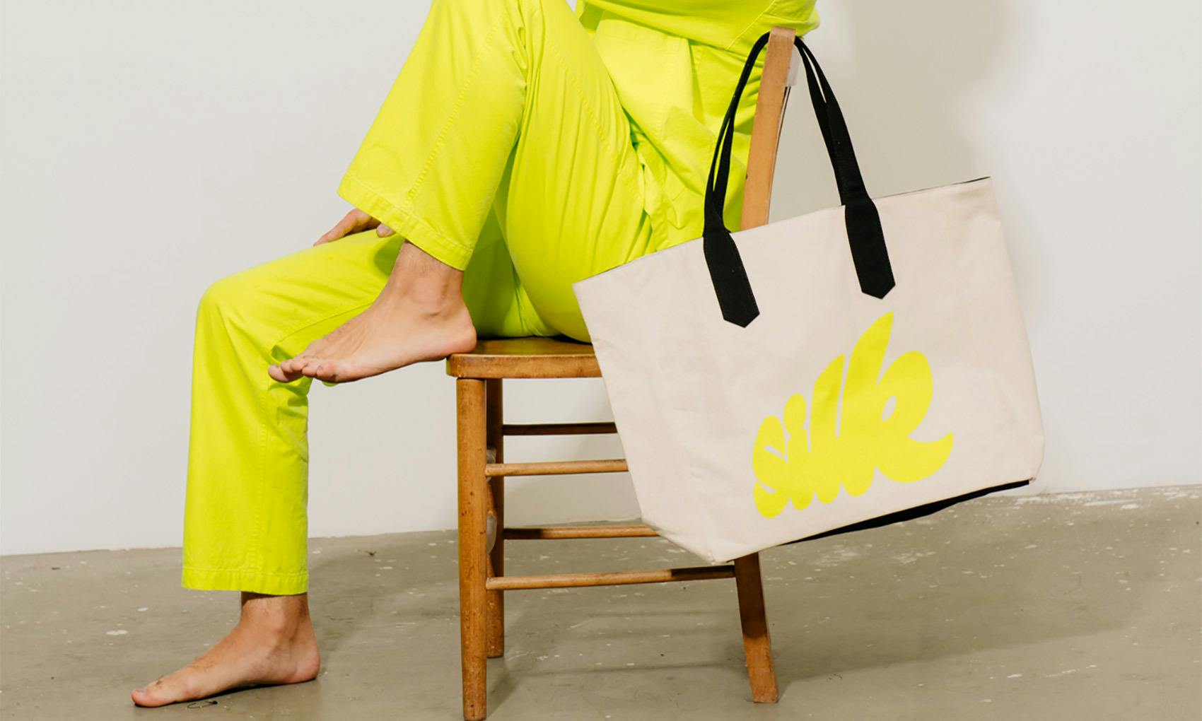 Model in yellow outfit, holding a bag that says silk