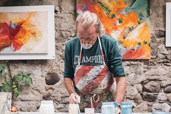 An older man painting glass in a studio