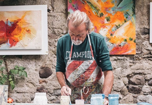 An older man painting glass in a studio