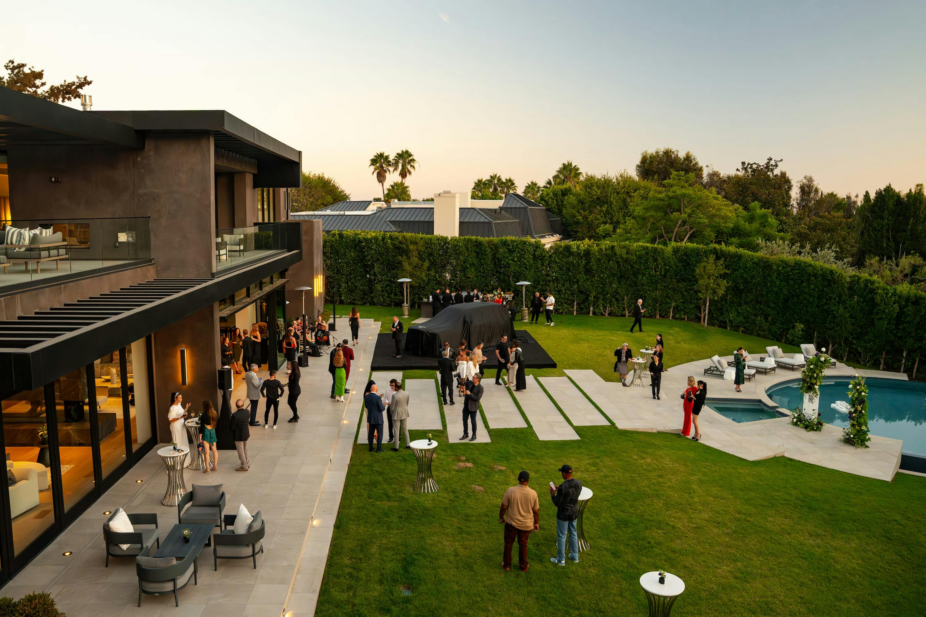 A shot of an outdoor event at sunset in front of a house with a pool.