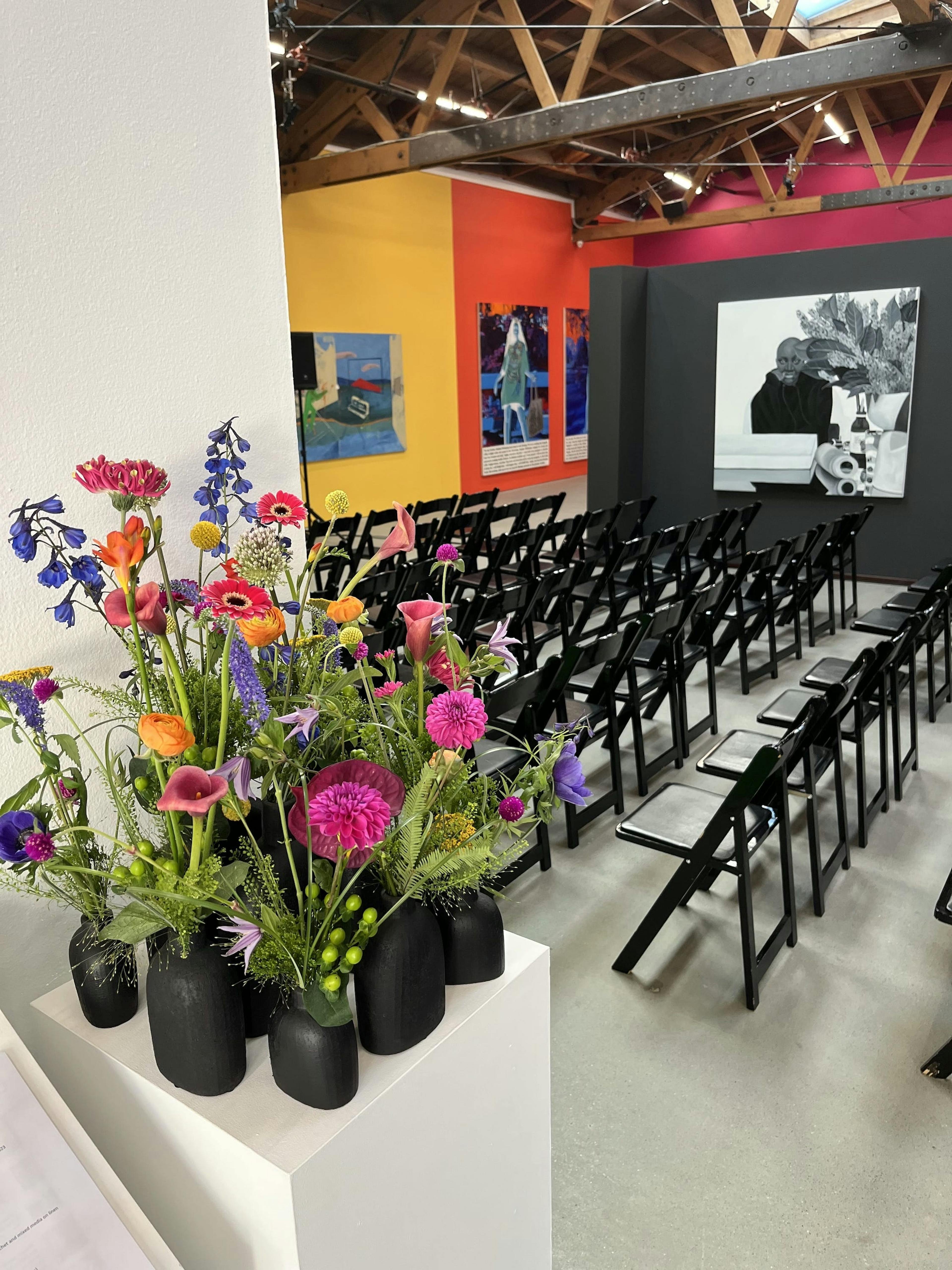 Arrangement of pink, yellow and purple flowers next to a gallery filled with black folding chairs. 