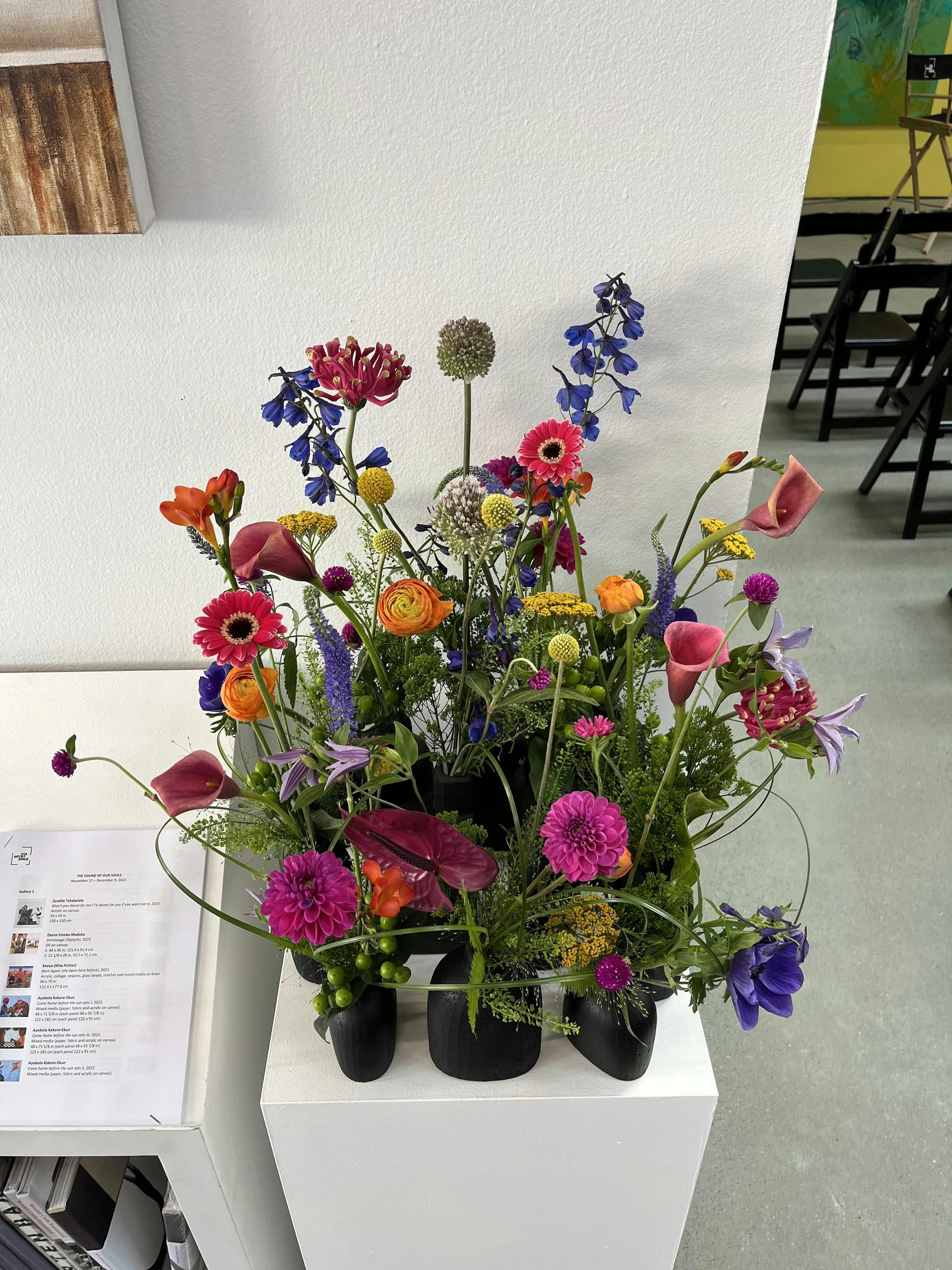 Arrangement of pink, yellow and purple flowers sitting on a white pedestal in a gallery.