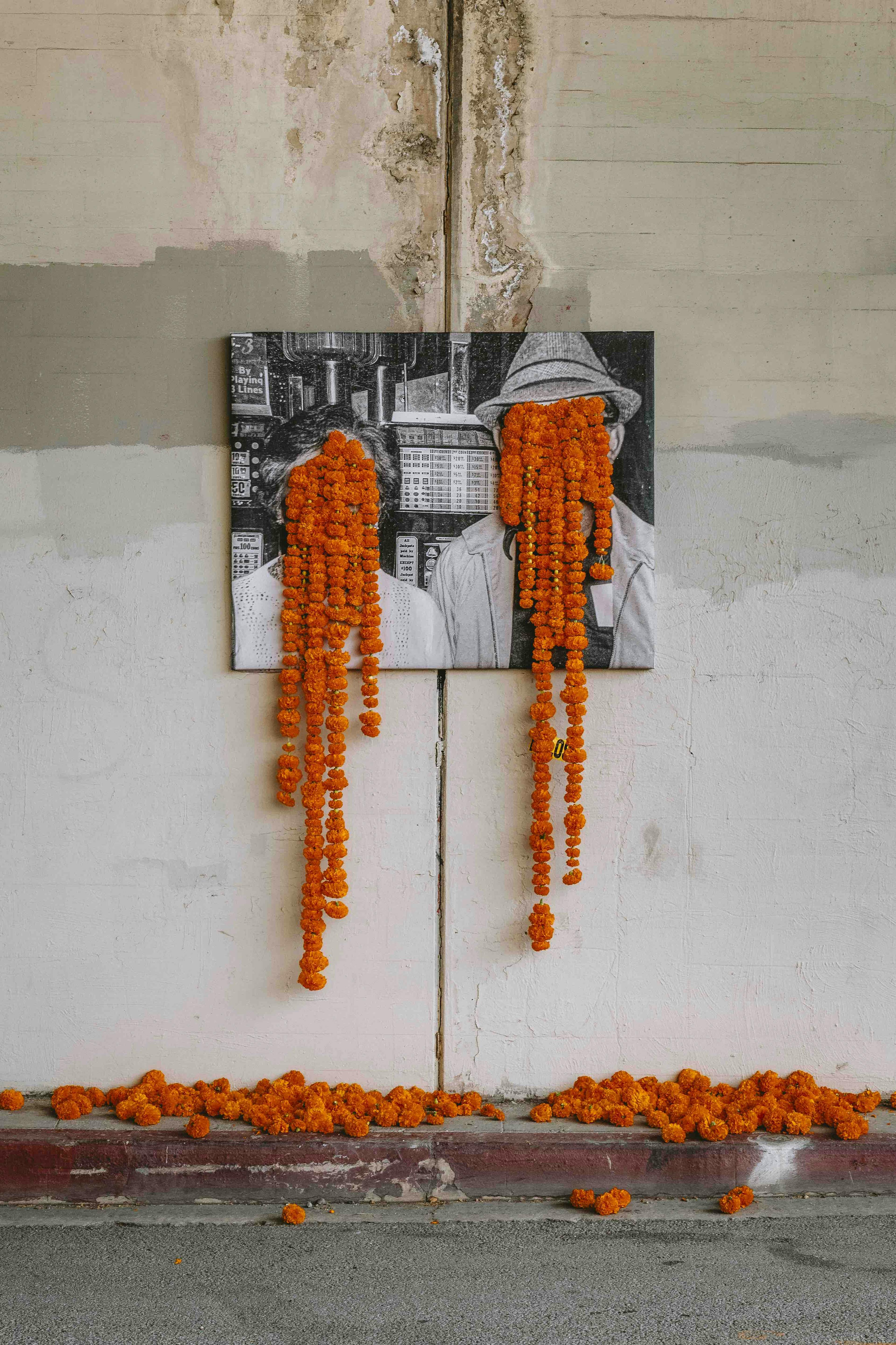 A floral art installation in an underpass with orange carnations dripping from the faces of a black and white photograph