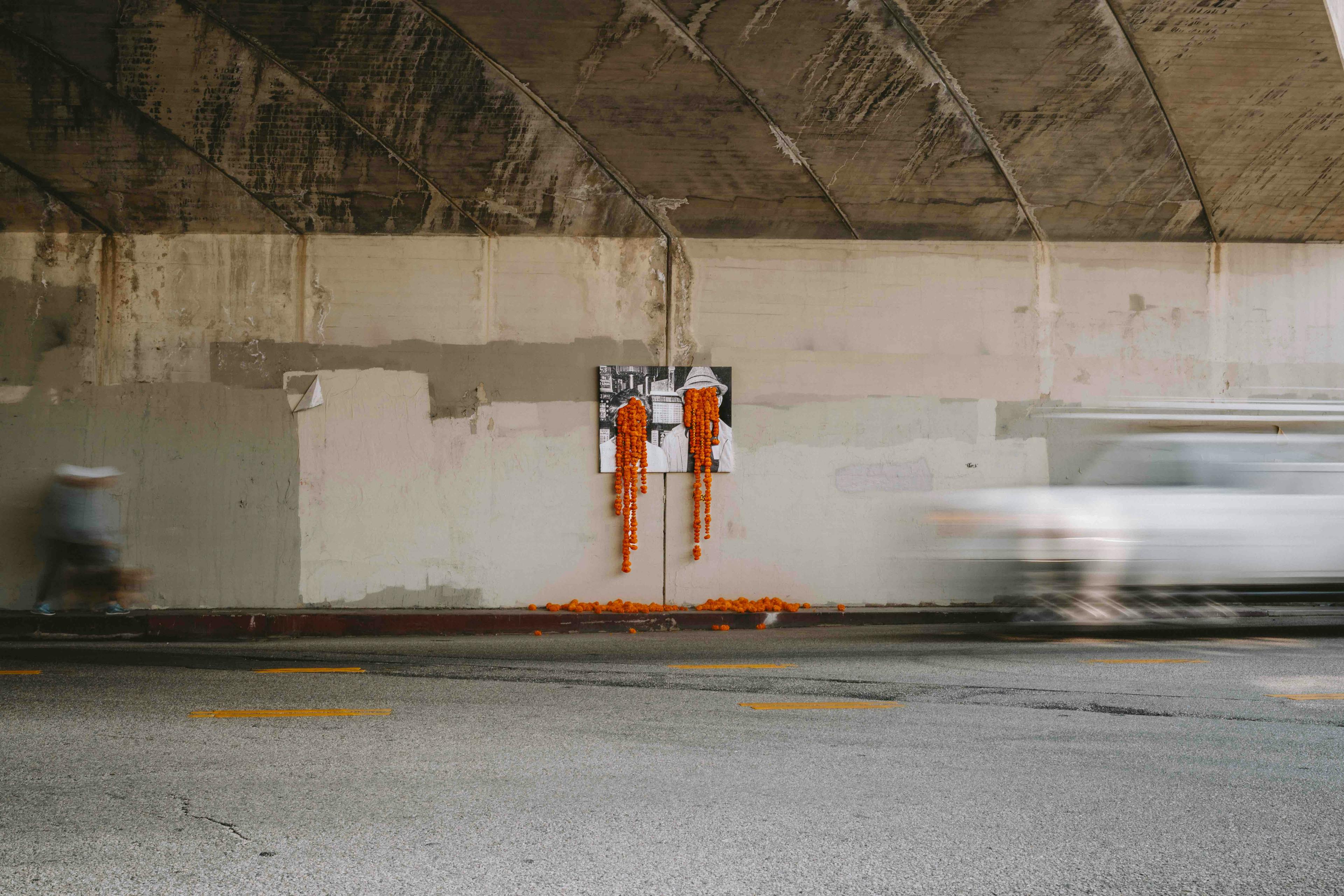 A floral art installation in an underpass with orange carnations dripping from two faces in a black and white photograph