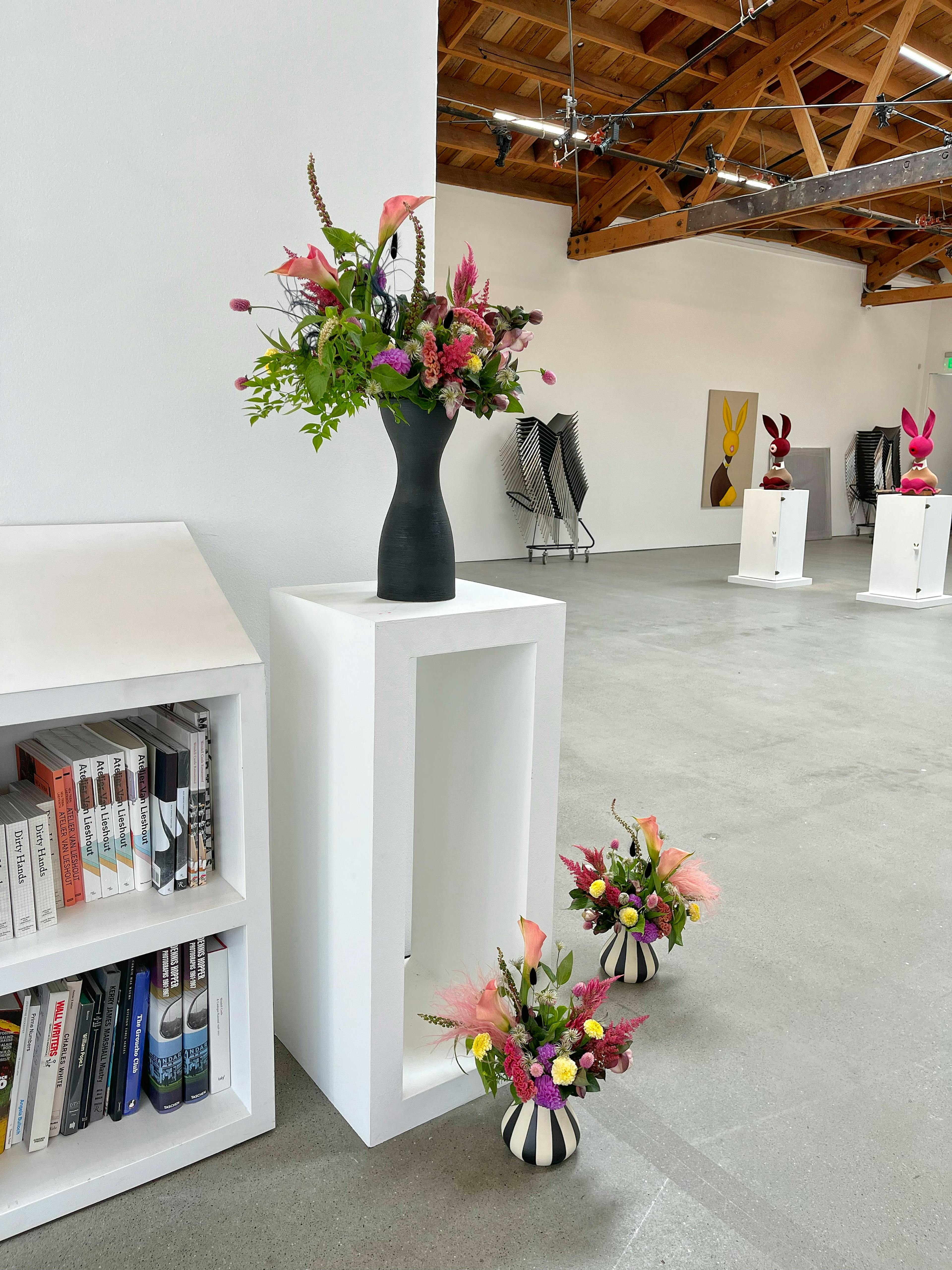 three arrangements of flowers, two with striped black and white vases and one with a tall black vase all with green and pink florals