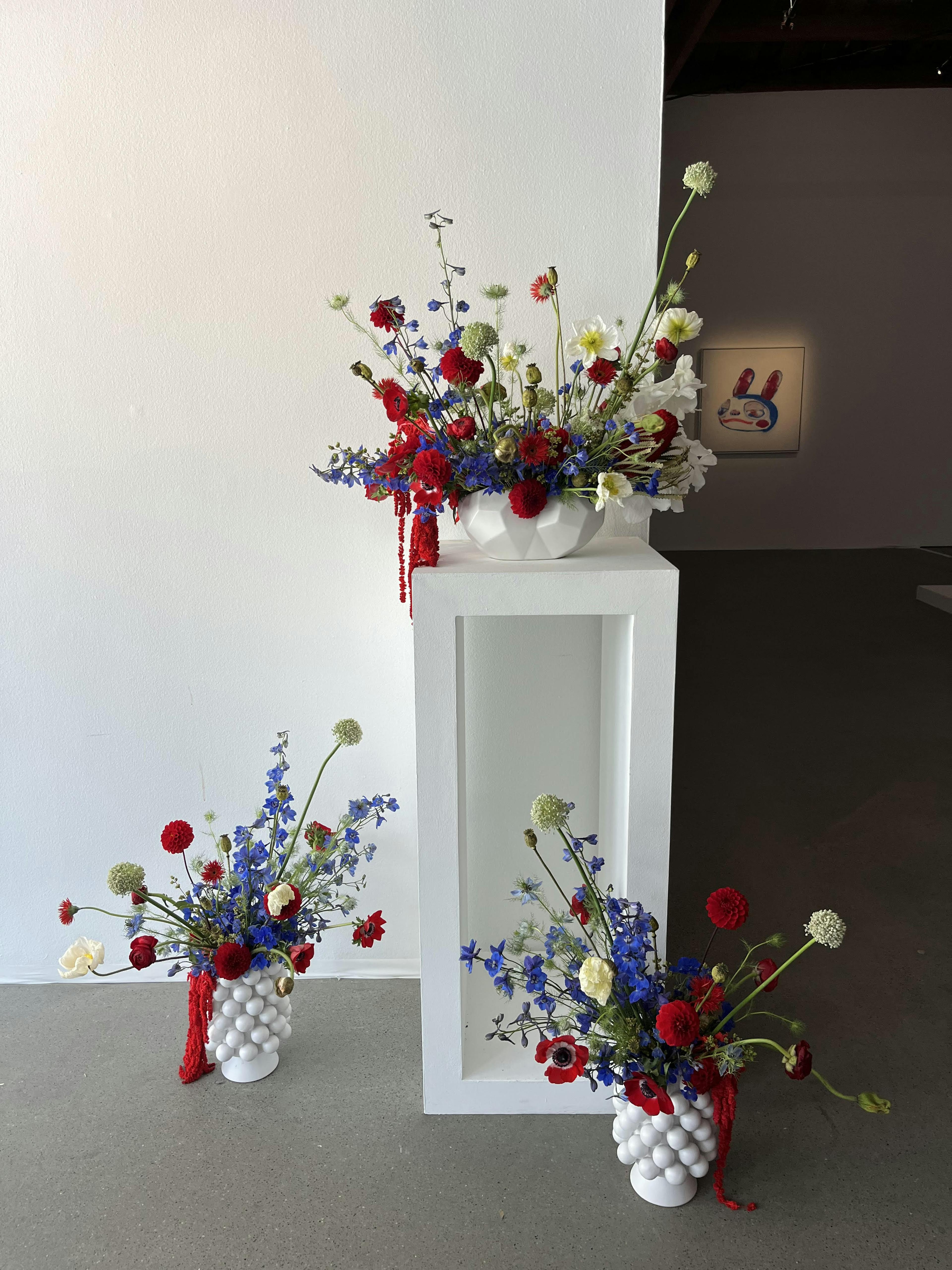 Three arrangements of red, purple and white flowers in white textured vases with one arrangement on a pedestal