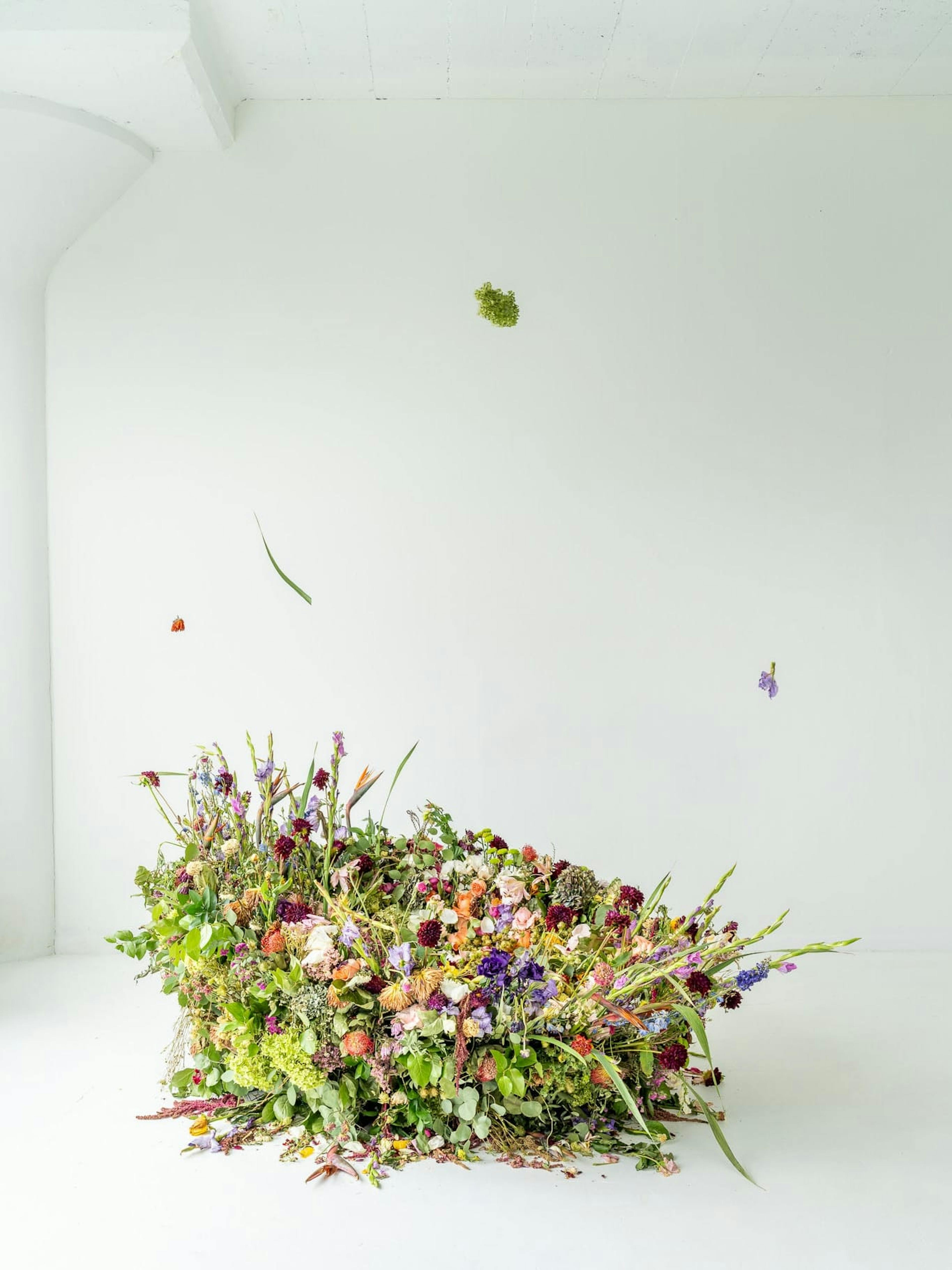 A colorful and textured arrangement of recycled flowers on the floor of a white room with a window. 