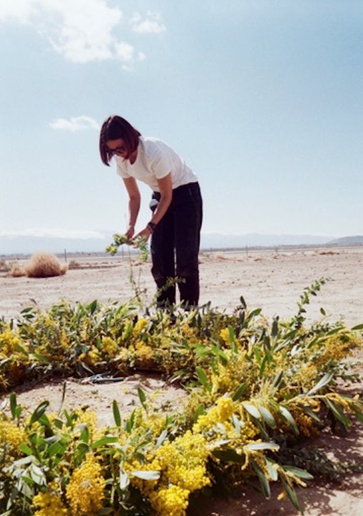 A women in the desert arranging yellow flowers on a round wooden frame.