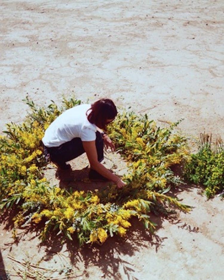 A women in the desert arranging yellow flowers on a round wooden frame.