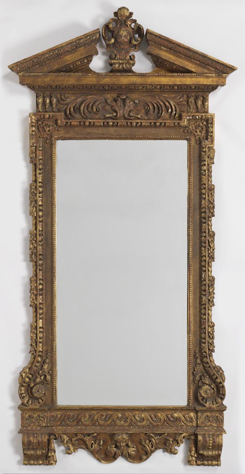 Antique mirror, circa 1910. Tall, rectangular, with carved cartouche and broken-triangular pediment on top, above the acanthus-decorated frieze, shaped base with putti below Vitruvian scroll banding. (Public Domain)