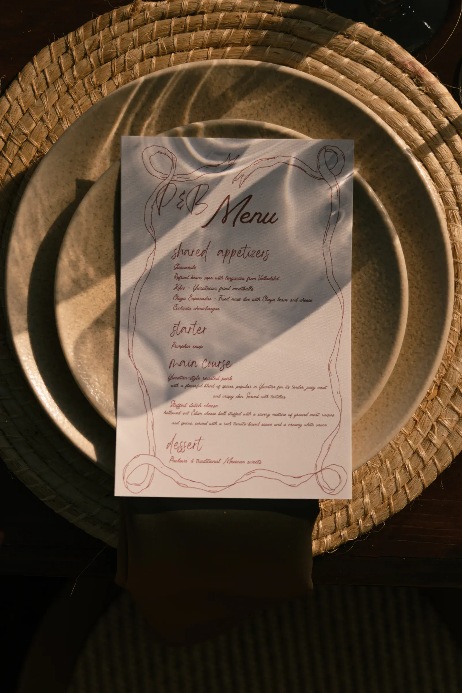 Un menú de papel con un elegante texto escrito a mano reposa sobre un mantel redondo tejido encima de un plato de cerámica rústica, lo que sugiere un ambiente de cena íntimo y acogedor.