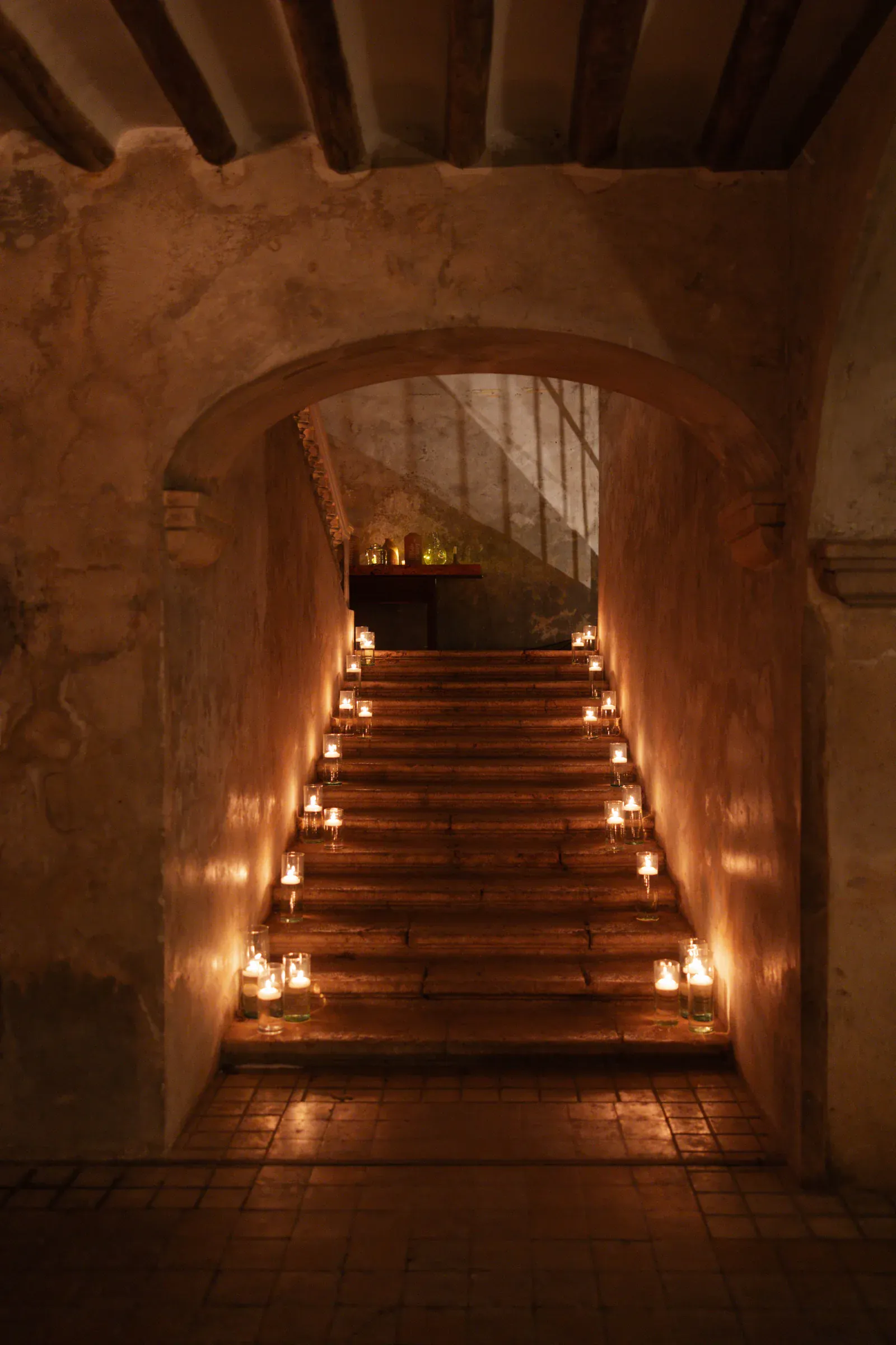 Una escalera de piedra tenuemente iluminada, adornada con velas en cada escalón, conduce a una puerta arqueada. La escena irradia un ambiente cálido y tranquilo.