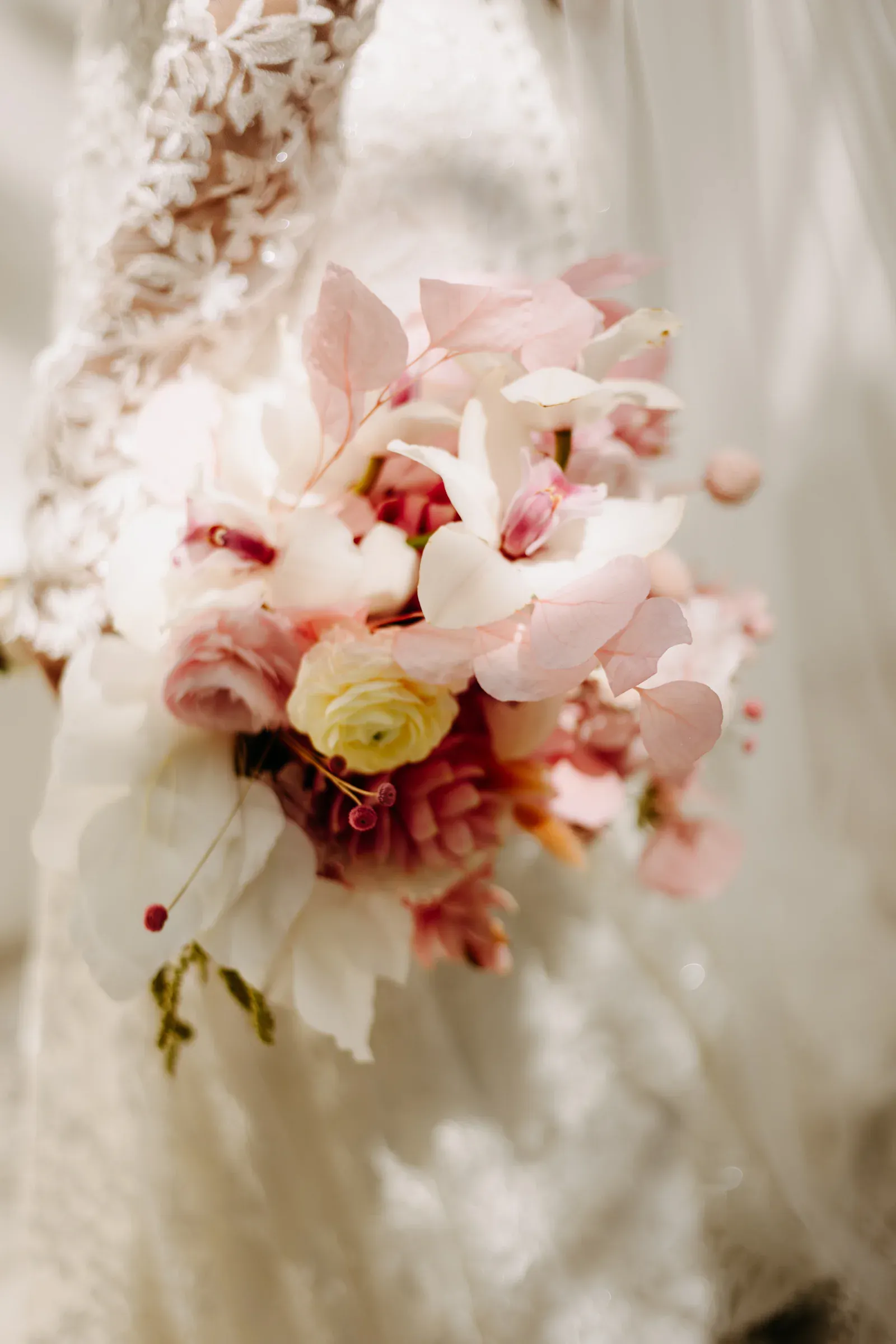 Primer plano de un ramo de novia con flores suaves en rosa y blanco, sostenido por una novia con una elegante manga de encaje. El tono es romántico y sereno.