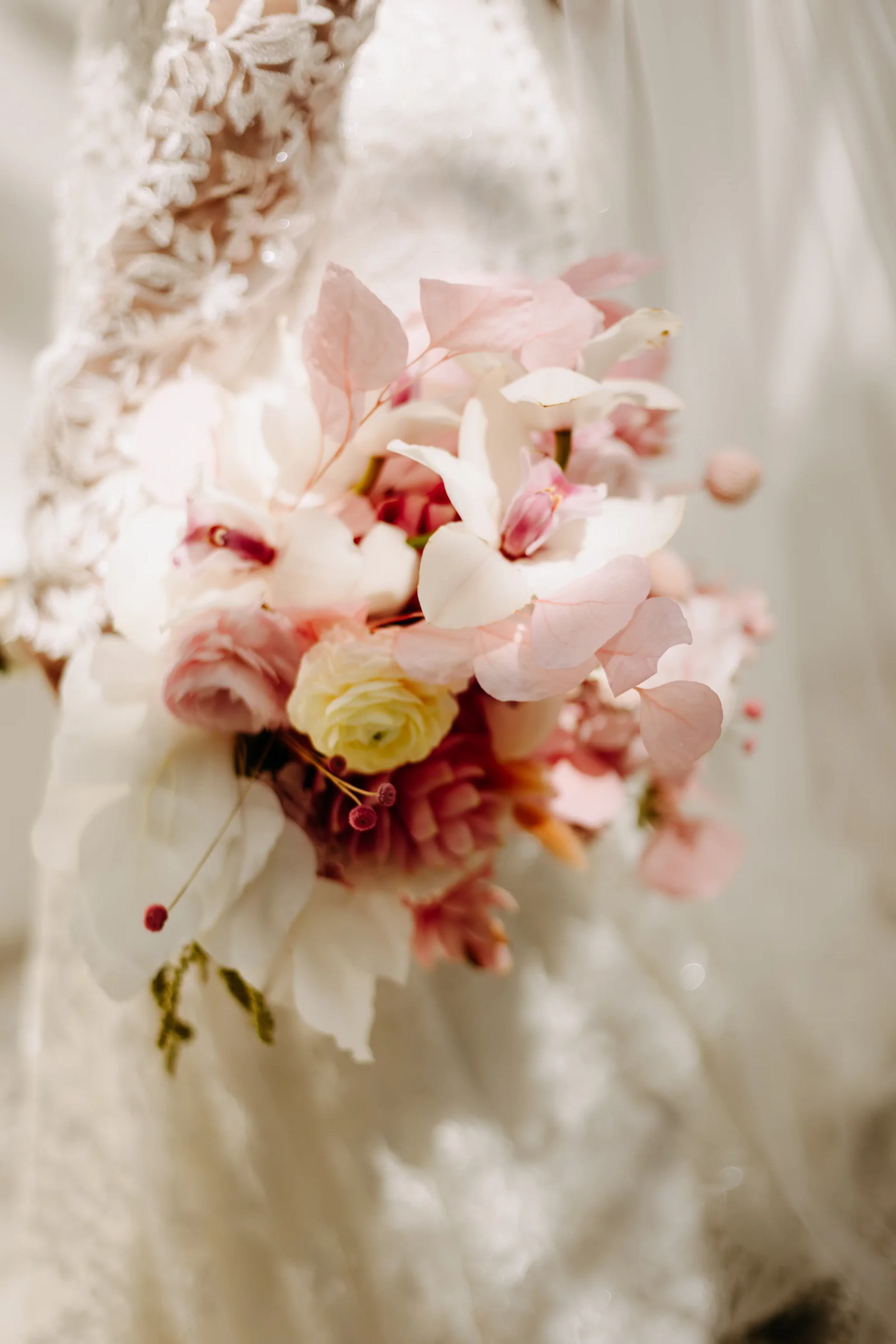 Primer plano de un ramo de novia con flores suaves en rosa y blanco, sostenido por una novia con una elegante manga de encaje. El tono es romántico y sereno.