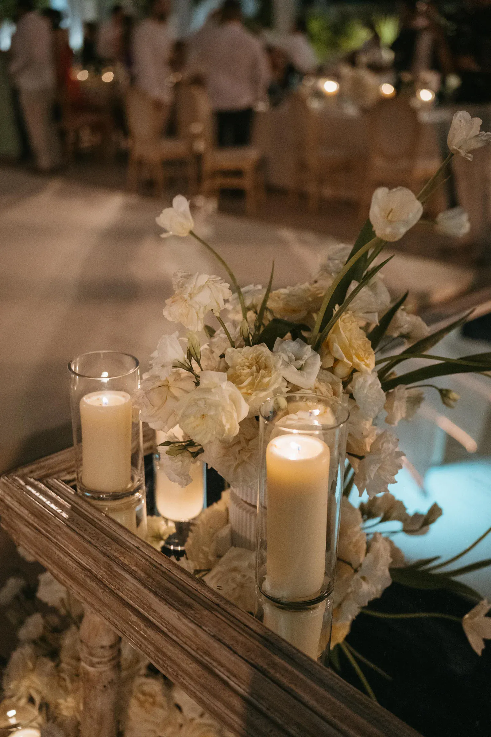 Un ambiente elegante con velas encendidas en candelabros de cristal y un jarrón de flores blancas sobre una mesa de madera. Un ambiente suave y cálido en una habitación con poca luz.