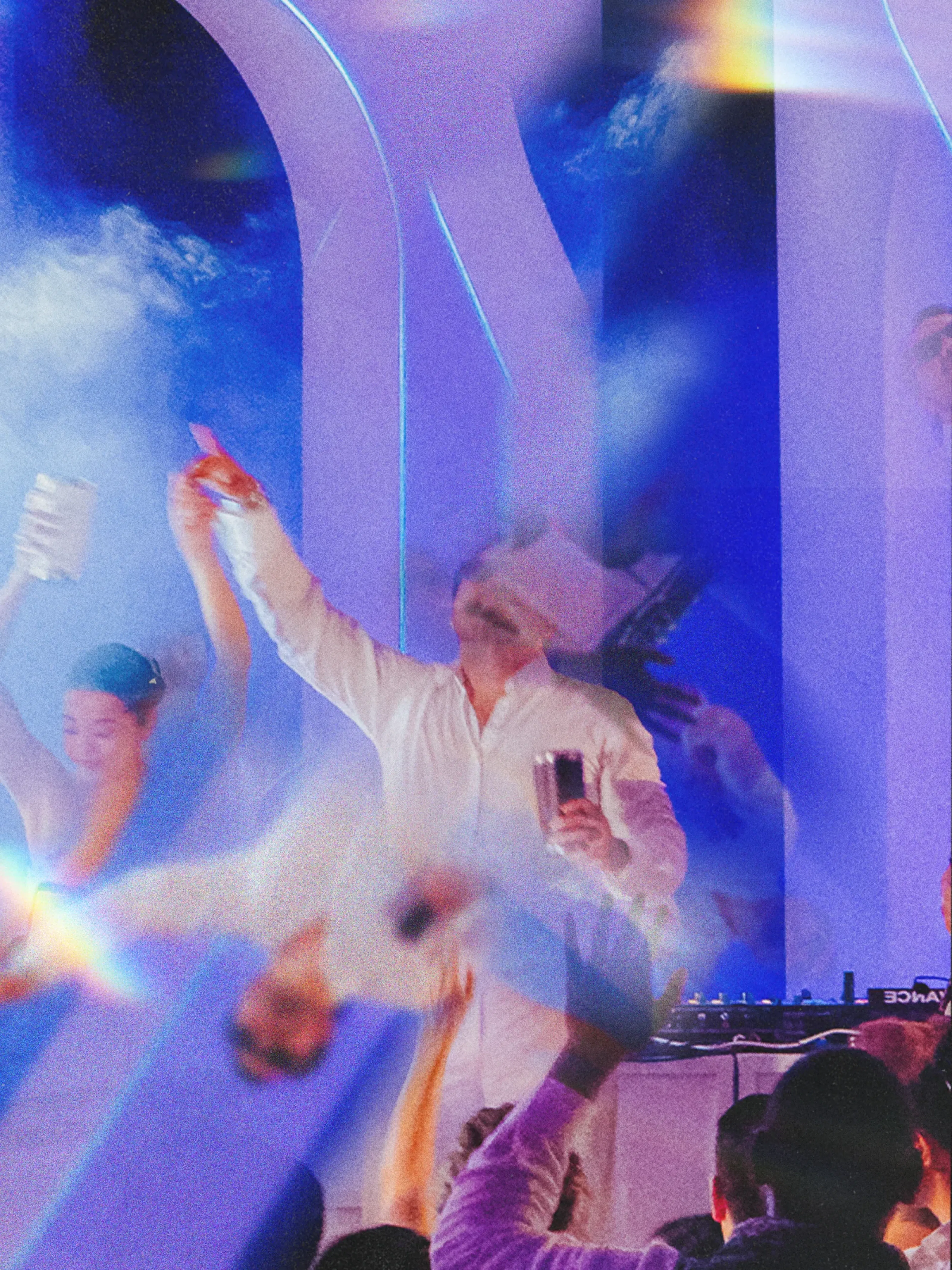 Una animada escena festiva presenta a una persona vestida de blanco bailando alegremente con una bebida en la mano. Las luces de colores y el humo crean un ambiente festivo y enérgico.